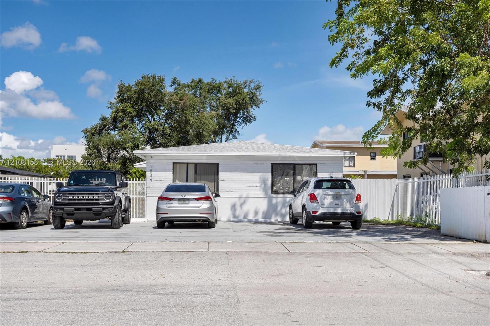 White masonry exterior with a low-slope roof, horizontal sliding windows, and a paved parking surface enclosed by fencing