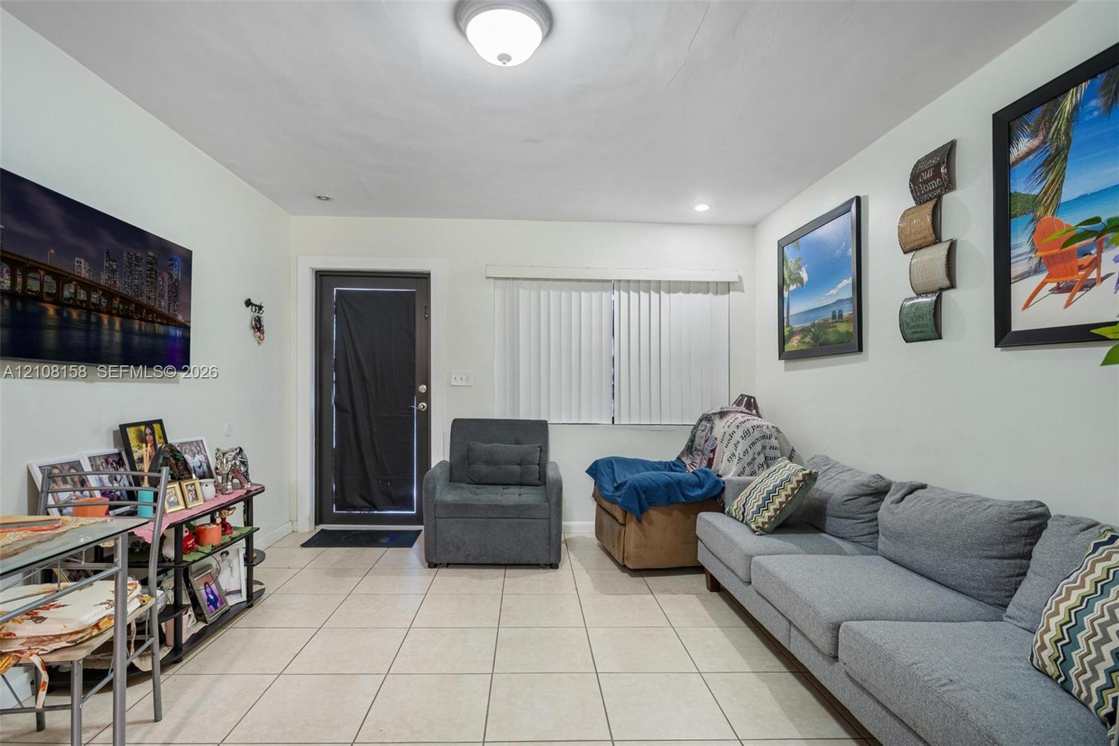 Light-toned ceramic tile flooring, neutral wall palette, single-light ceiling fixture, and vertical window blinds