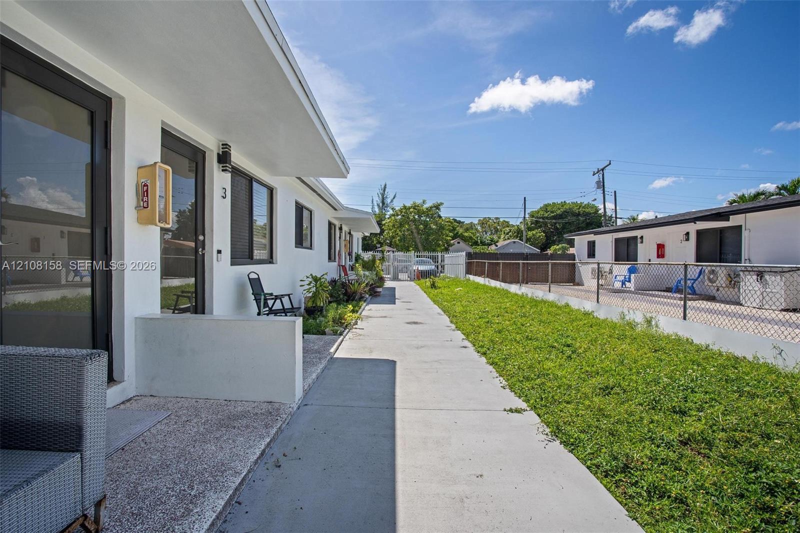 Concrete walkway lined with a grass lawn, metal fencing, and white exterior building facades featuring glass-panel doors