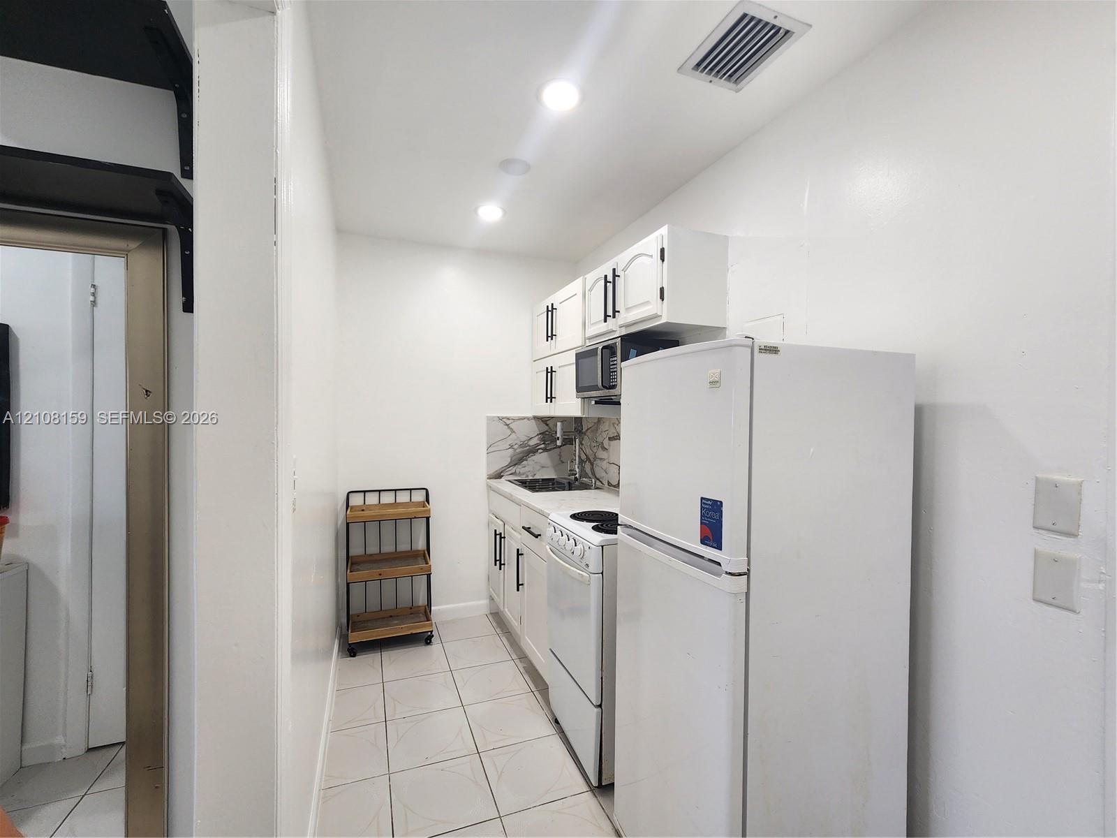Kitchen featuring white cabinetry with dark hardware, patterned stone-finish backsplash, recessed lighting, and tile flooring