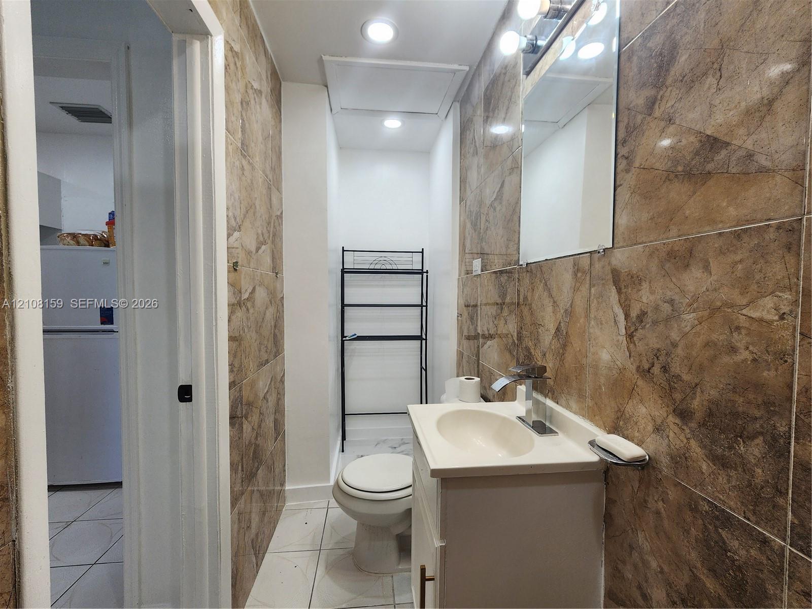 Bathroom featuring floor-to-ceiling large-format tile walls, recessed lighting, vanity with a modern faucet, and white tile flooring