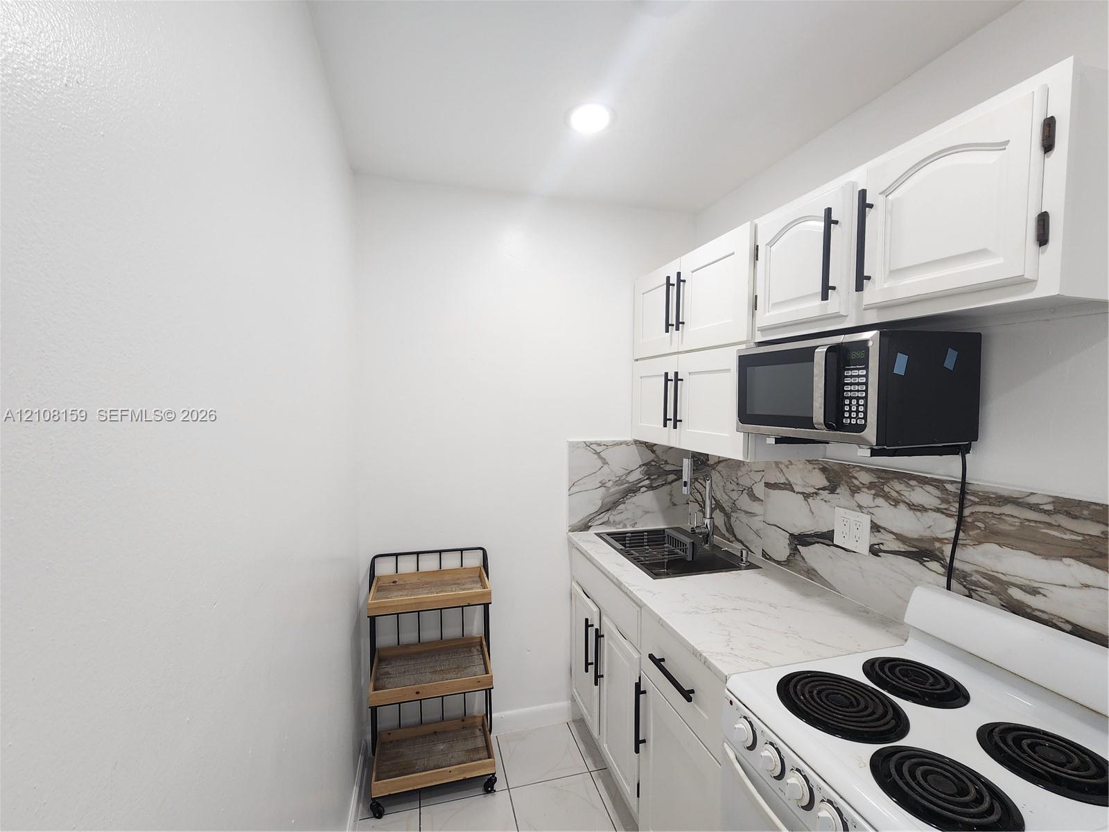 Kitchen featuring white cabinetry with matte black hardware, stone-patterned backsplash, light-toned countertop, integrated sink, and white electric range