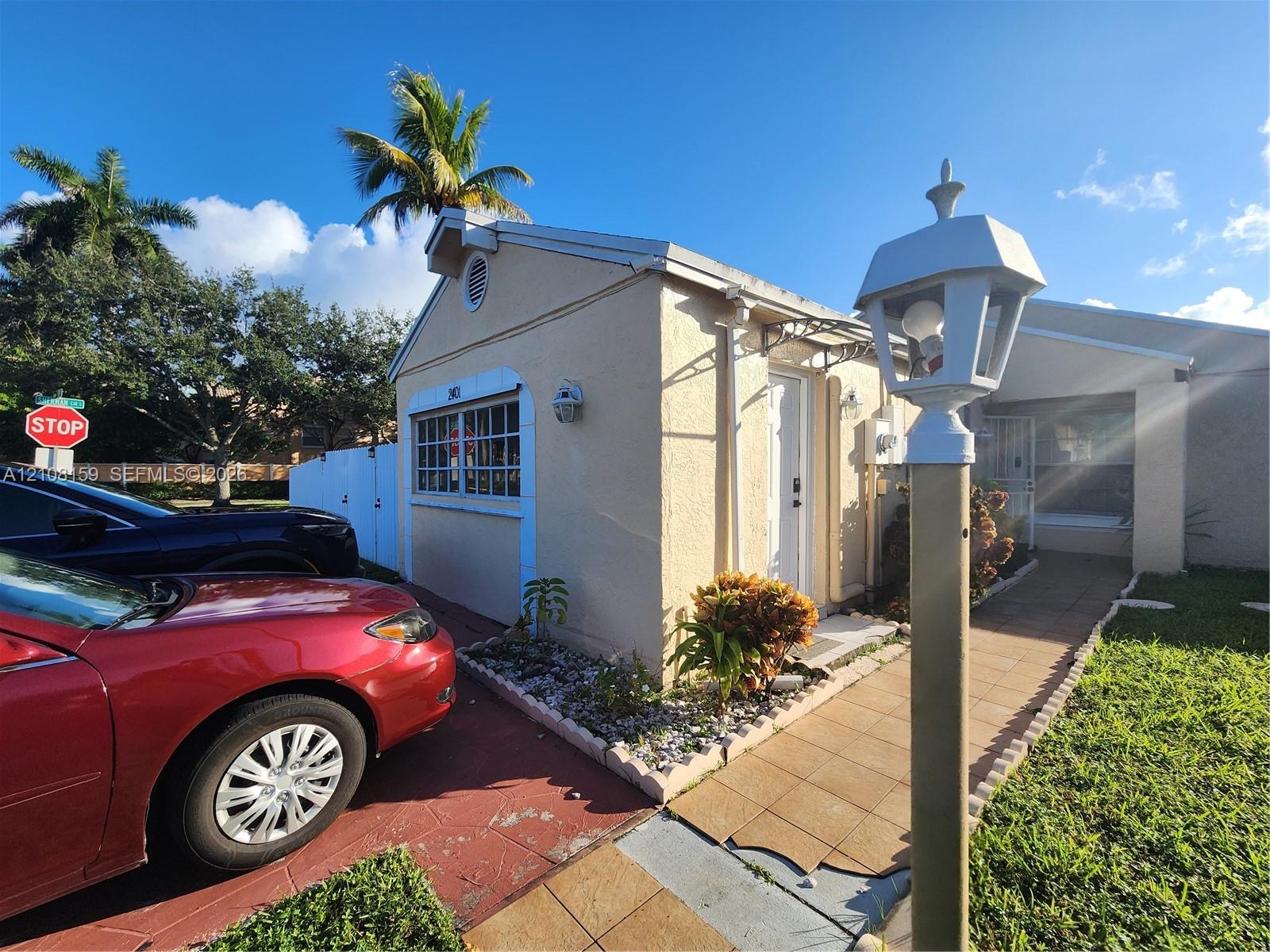 Stucco exterior featuring decorative window trim, a paved walkway, a standalone lamp post, and low-maintenance stone landscaping
