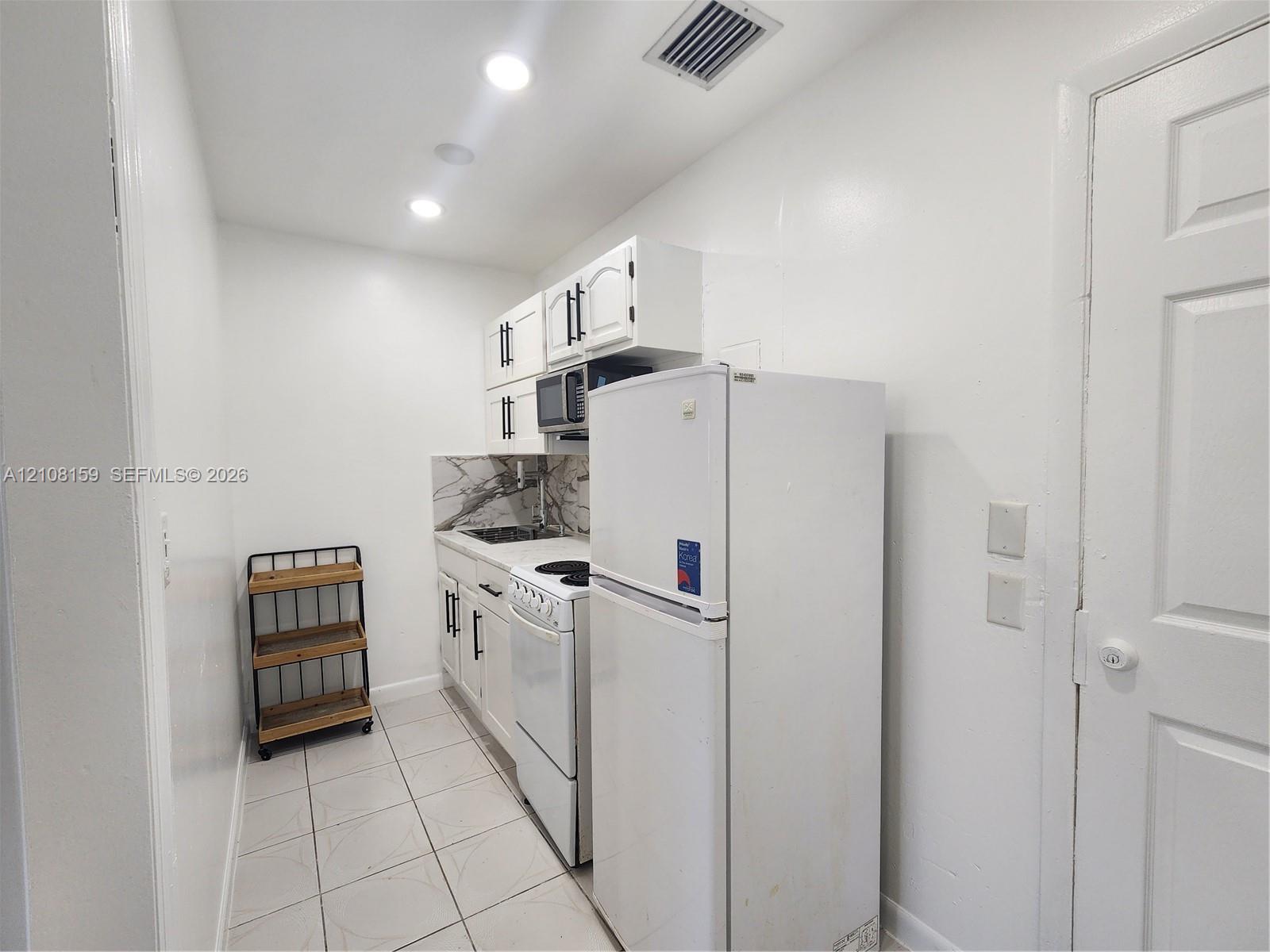 Kitchen featuring white cabinetry with matte black hardware, stone-finish backsplash, built-in range, and tile flooring