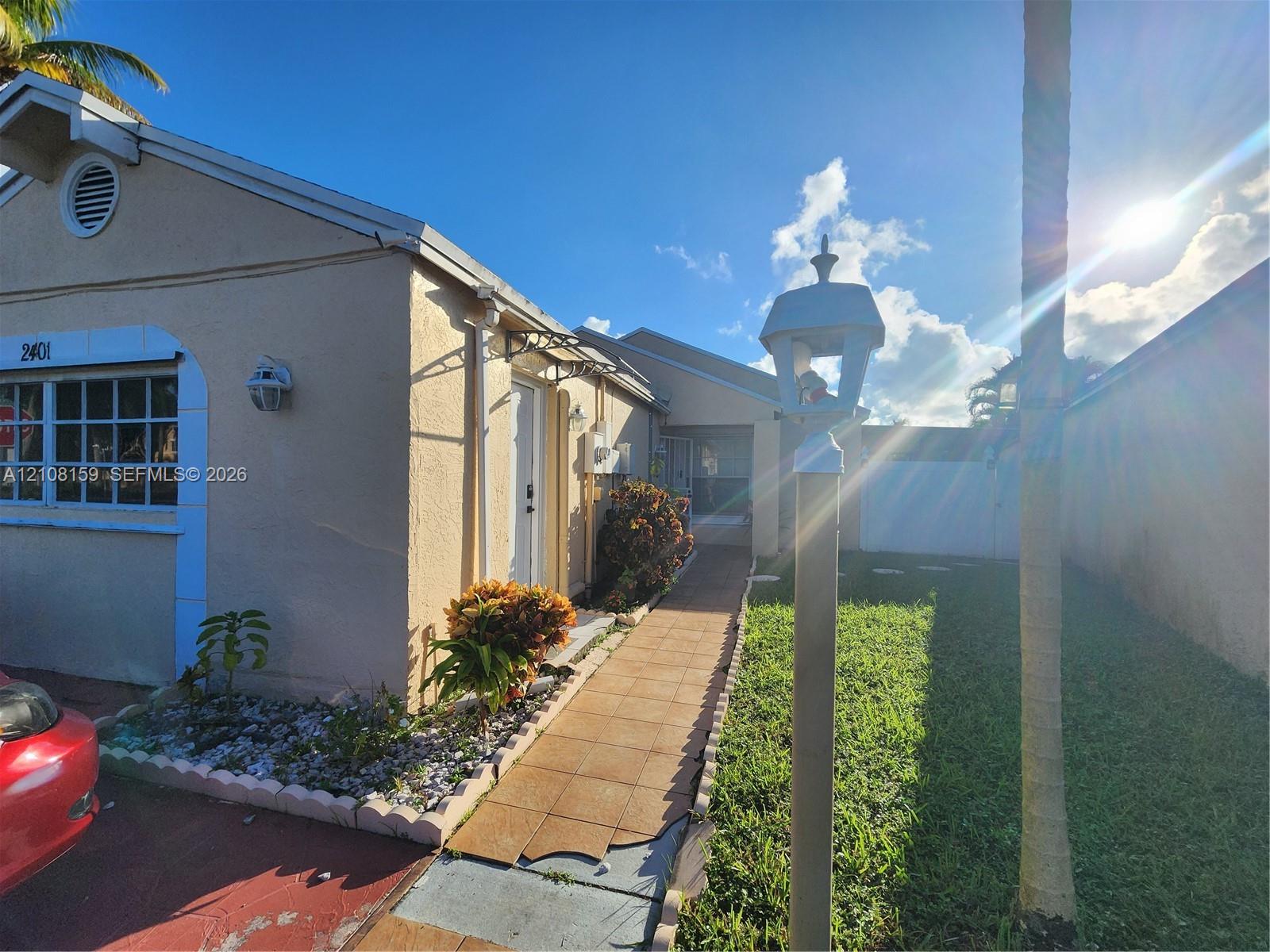Exterior featuring a stucco facade, a tile-paved walkway, and a decorative post lamp