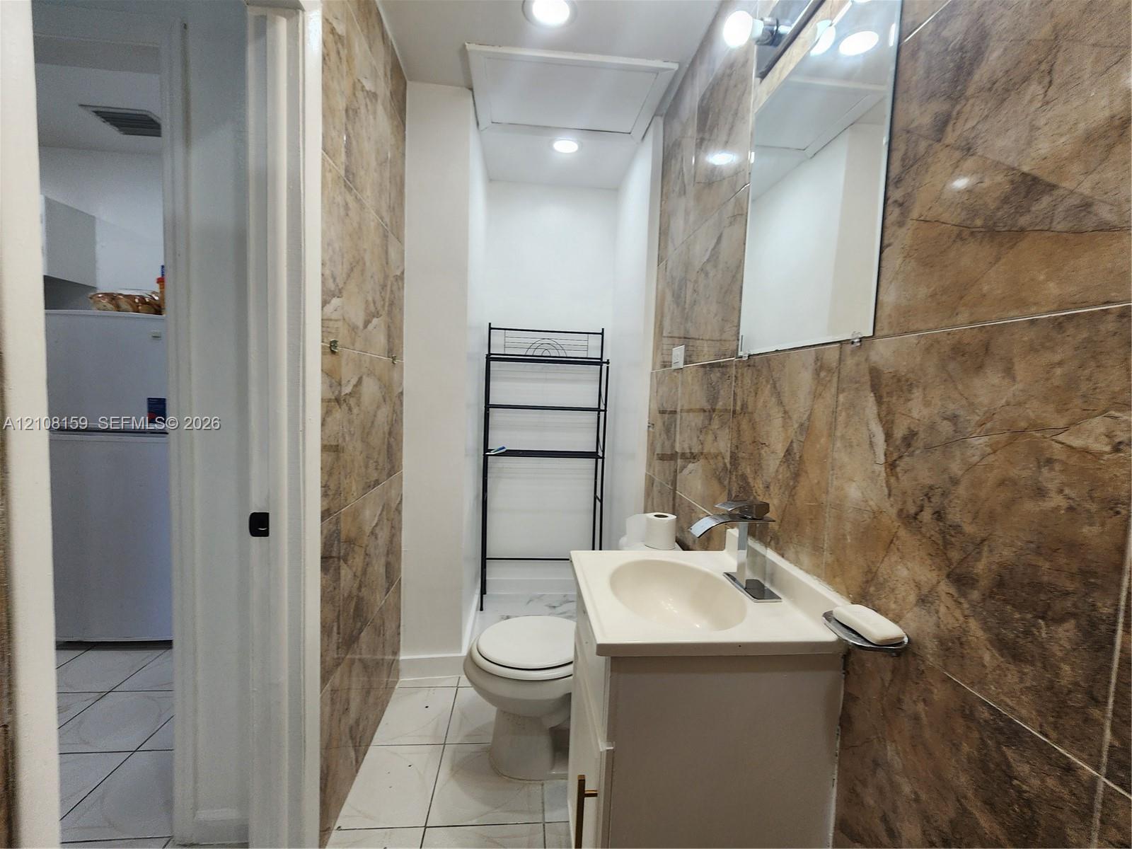 Bathroom featuring floor-to-ceiling large-format tile walls, white tile flooring, a built-in vanity with a sink, and a wall-mounted mirror