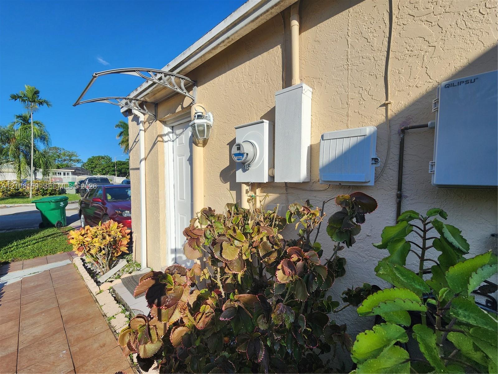 Stucco exterior featuring a metal door awning, exterior wall-mounted light fixture, and tiled walkway