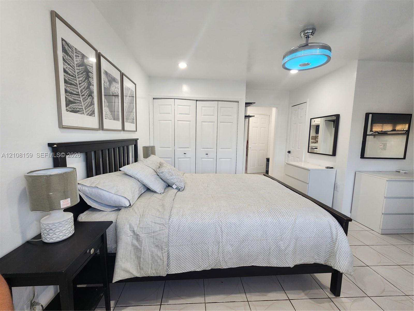 Bedroom featuring white tile flooring, multi-panel bi-fold closet doors, and a ceiling-mounted modern circular light fixture with integrated fan
