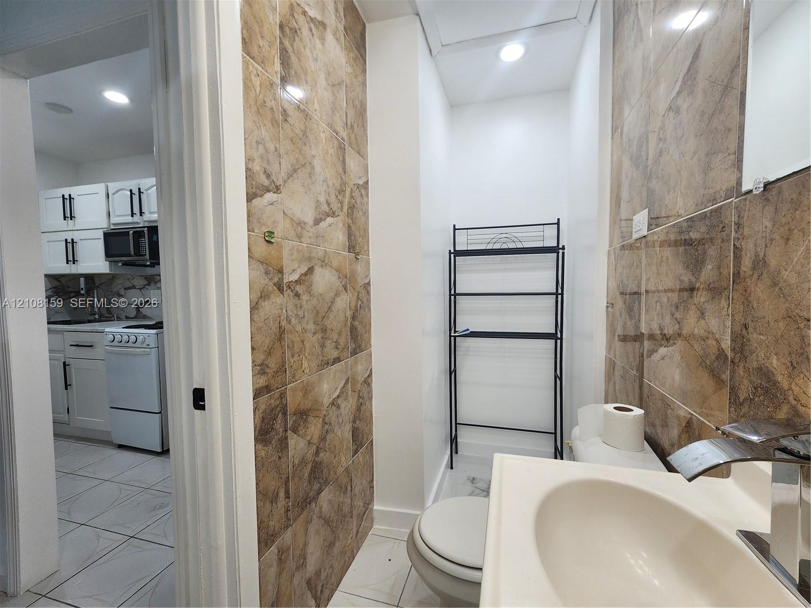 Bathroom featuring floor-to-ceiling tile surrounds, a pedestal sink with a modern faucet, and recessed lighting