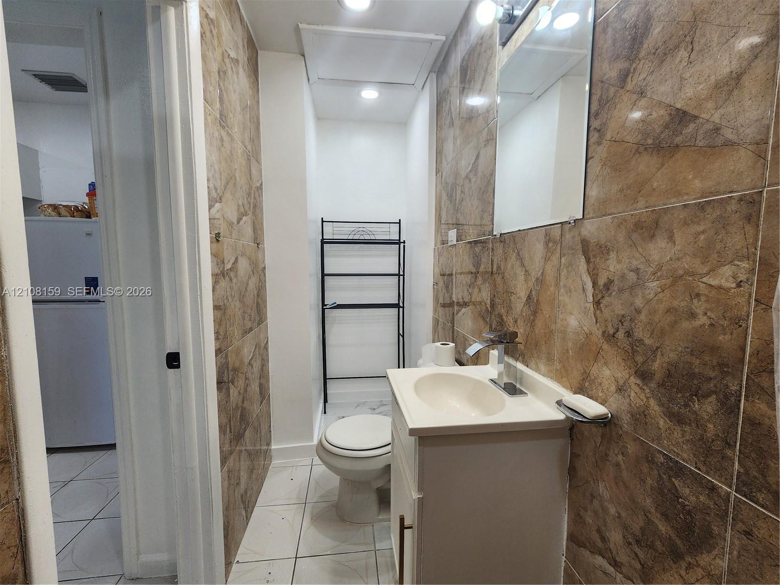 Bathroom featuring floor-to-ceiling stone-patterned wall tile, white vanity cabinet with integrated sink, chrome faucet, and recessed lighting