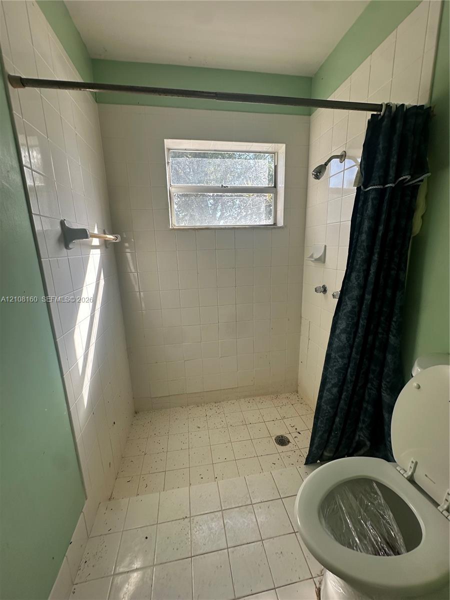 Walk-in shower enclosure featuring white square tile surround, integrated soap dish, chrome shower head, and central window