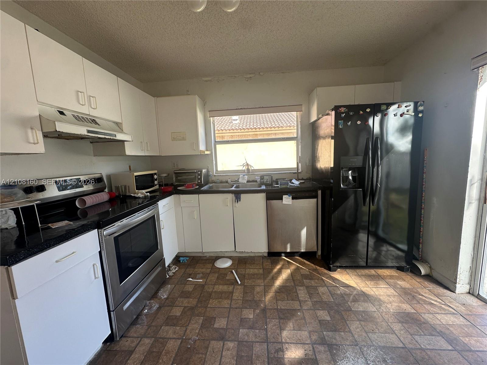 Kitchen featuring white cabinetry, dark countertops, a stainless steel range and dishwasher, and a black refrigerator