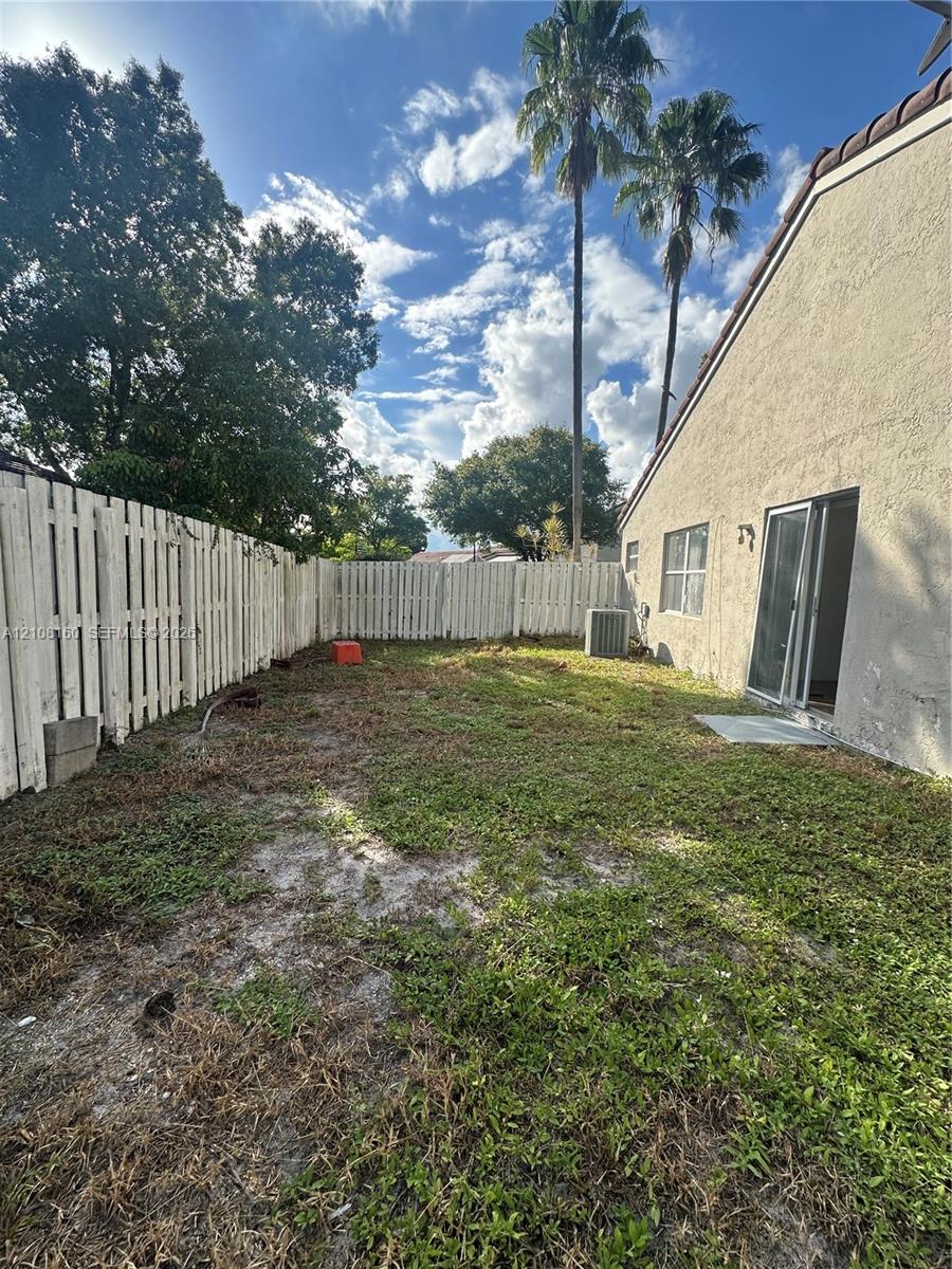 Private backyard featuring a stucco exterior, vertical panel fencing, and mature palm trees