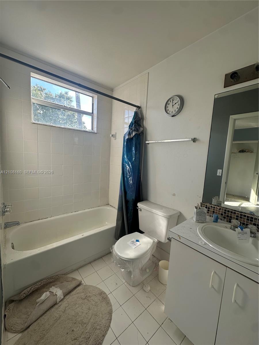 Bathroom featuring white tiled tub surround, rectangular window, vanity with integrated basin, mosaic tile backsplash, and wall-mounted vanity mirror