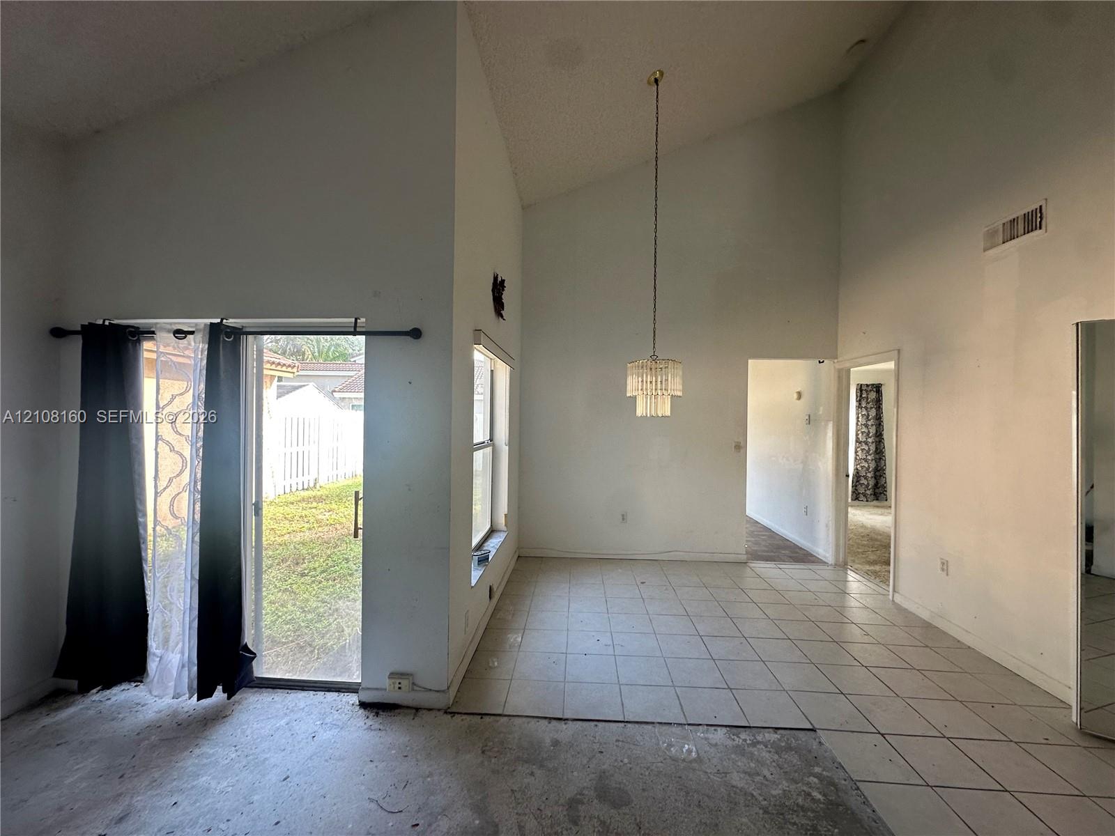 Vaulted ceilings featuring a suspended tiered chandelier, large window, and sliding glass door with exterior access