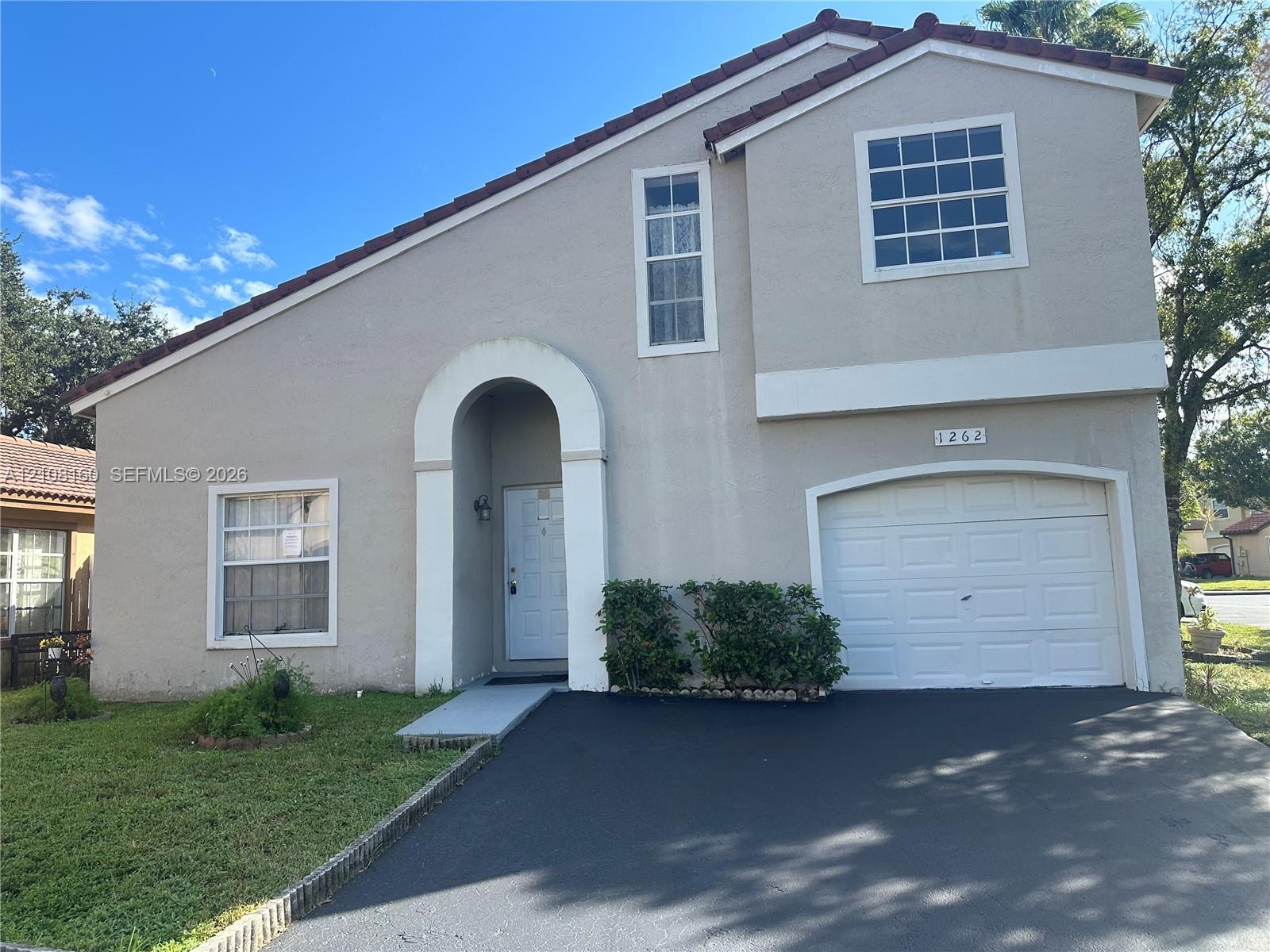 Two-story exterior featuring a stucco facade, tiled roof, arched entryway, and an attached single-car garage