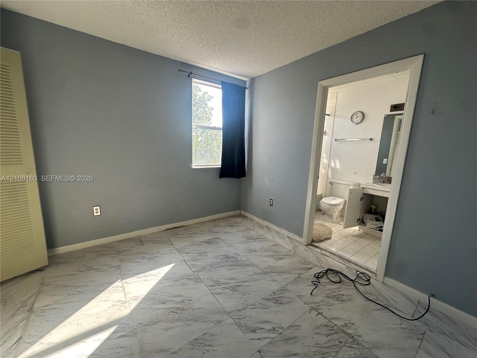 Large-format tile flooring, louvered-panel closet door, and single-pane window with natural lighting