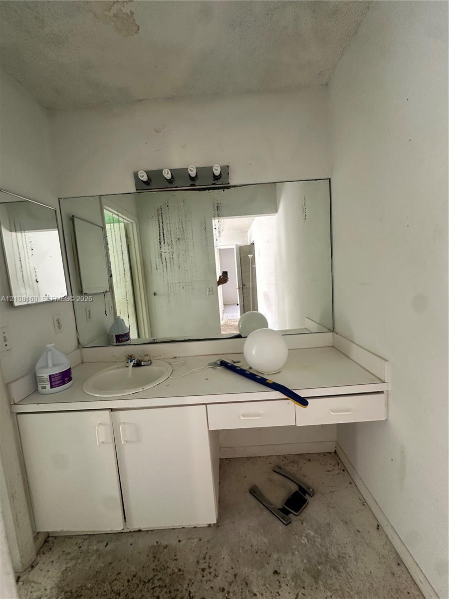 Built-in vanity featuring white cabinetry, integrated sink, and an expansive wall-mounted mirror with a multi-bulb light fixture