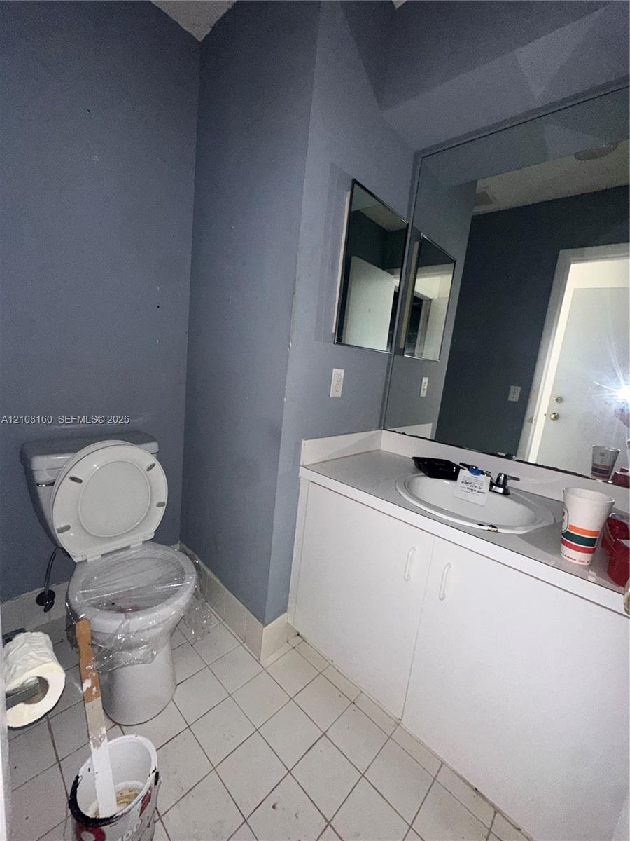 Bathroom featuring a white vanity cabinet, solid-surface countertop with an integrated oval sink, single-handle faucet, large wall-mounted mirror, and tile flooring