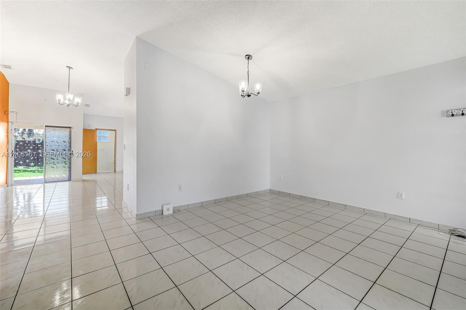 Interior space featuring light-colored tile flooring, neutral walls, two decorative multi-light chandeliers, and sliding glass door access to the exterior