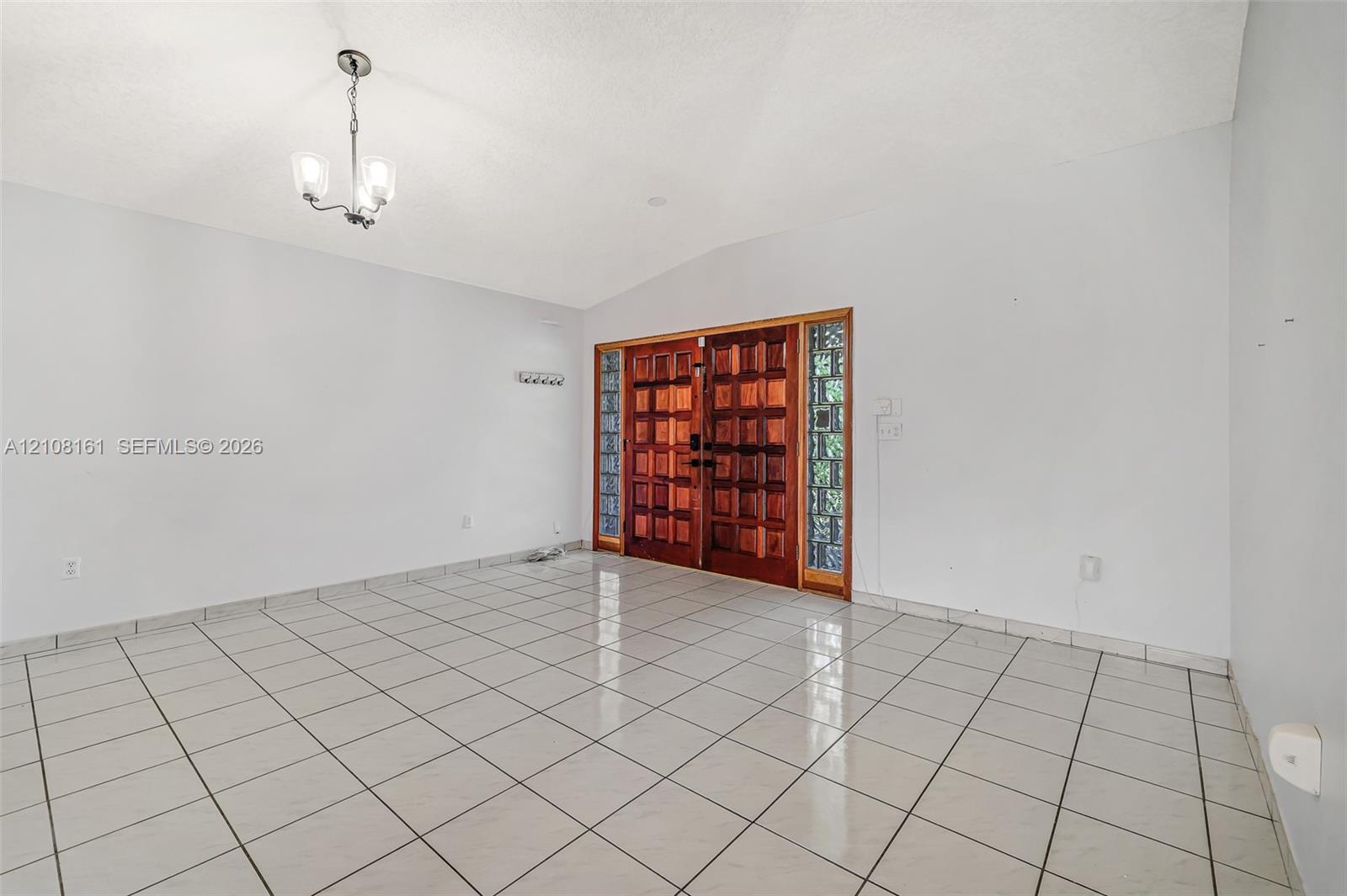 Entryway featuring ceramic tile flooring, vaulted ceilings, dual wood-finish doors, glass block sidelights, and a tiered metal chandelier