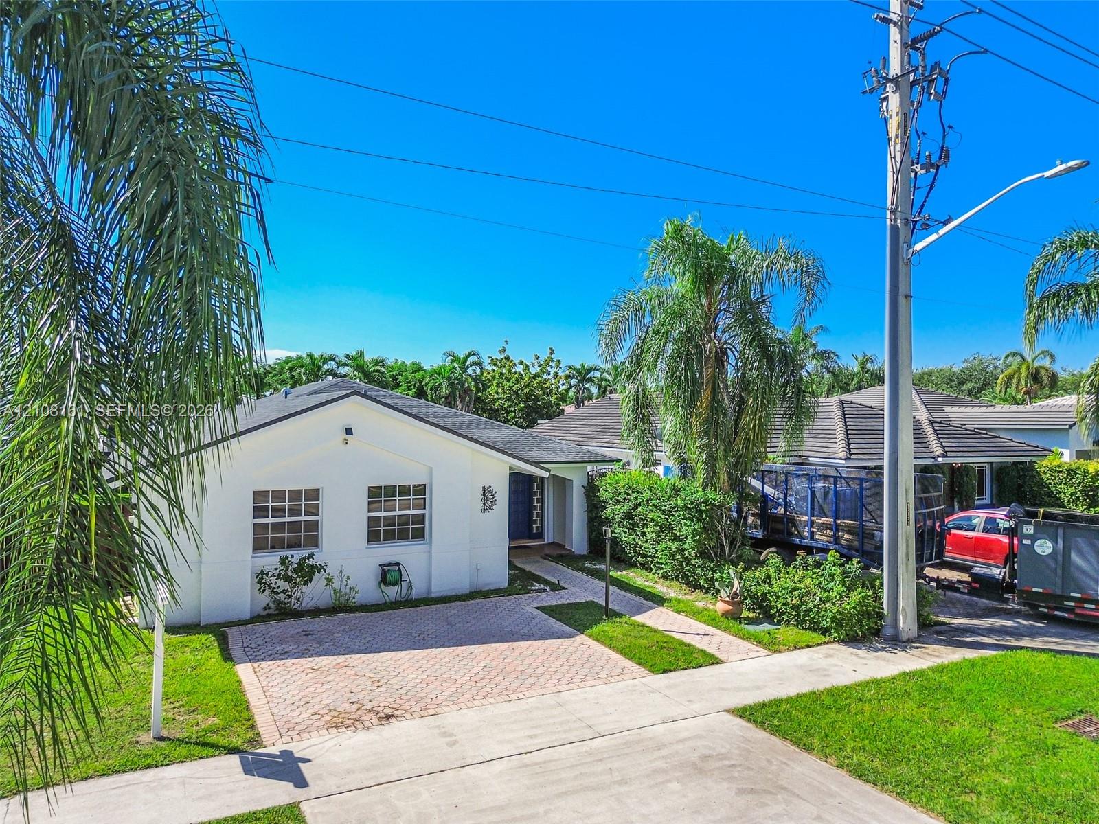 Single-story residence featuring a white stucco exterior, multi-hipped roof, paved driveway, and established landscape