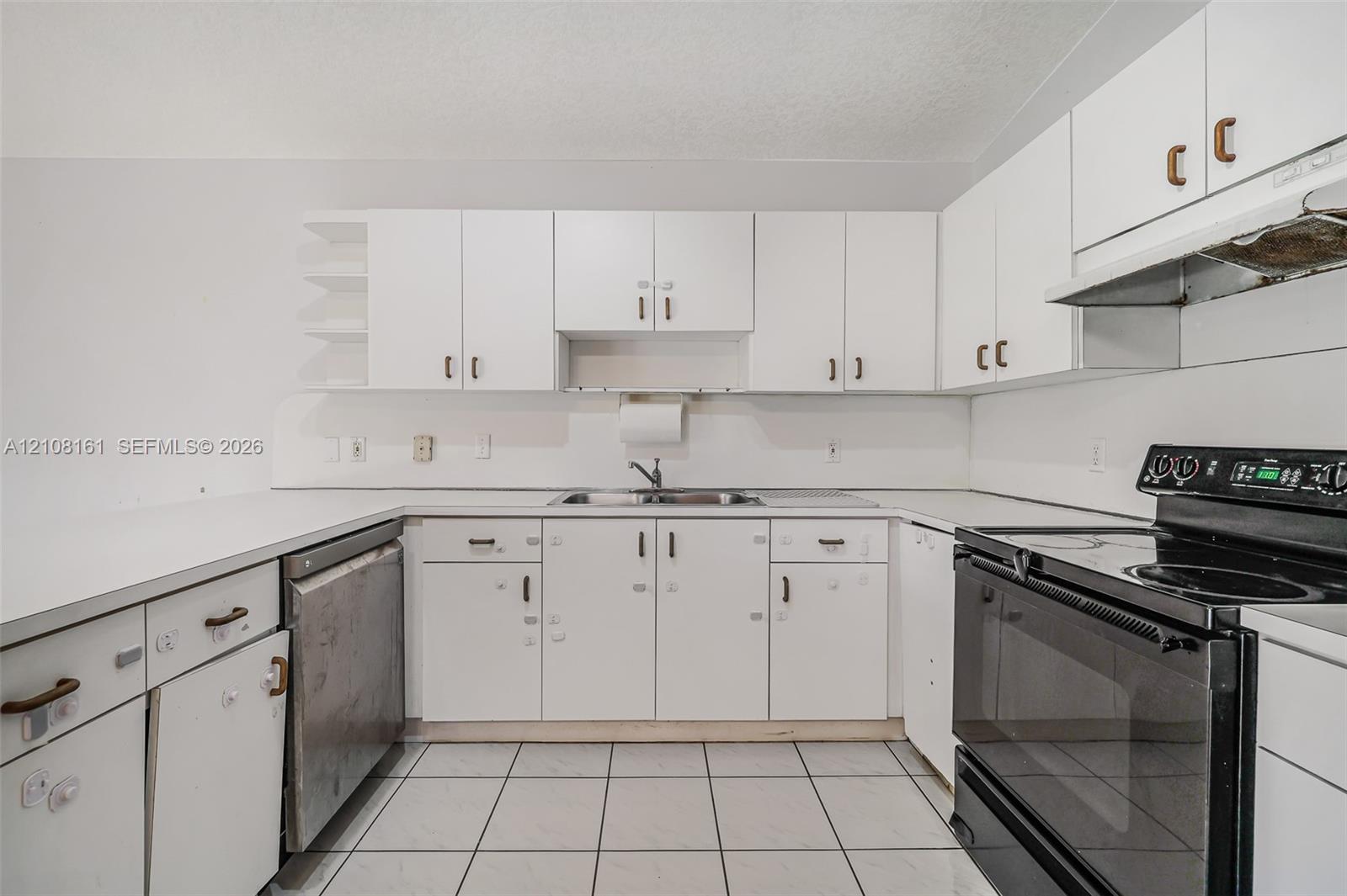 Kitchen featuring white cabinetry, solid-surface countertops, dual-basin stainless steel sink, tile flooring, and integrated black appliance suite
