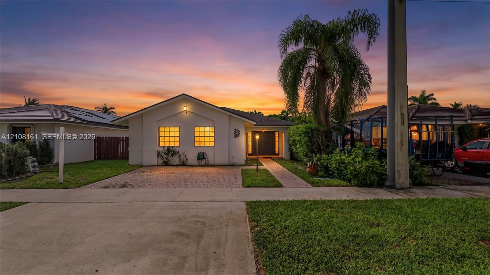 Single-story exterior featuring a light-toned stucco faade, paver driveway, covered entryway, and mature palm tree