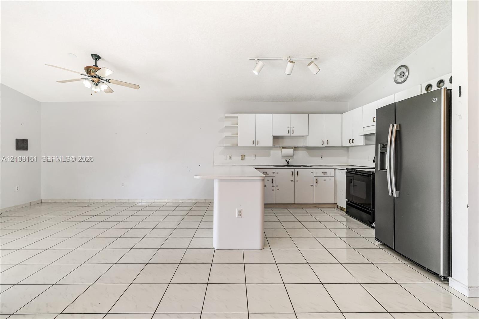 Kitchen featuring white cabinetry, an island with an extended countertop, large-format tile flooring, a stainless steel side-by-side refrigerator, and track lighting