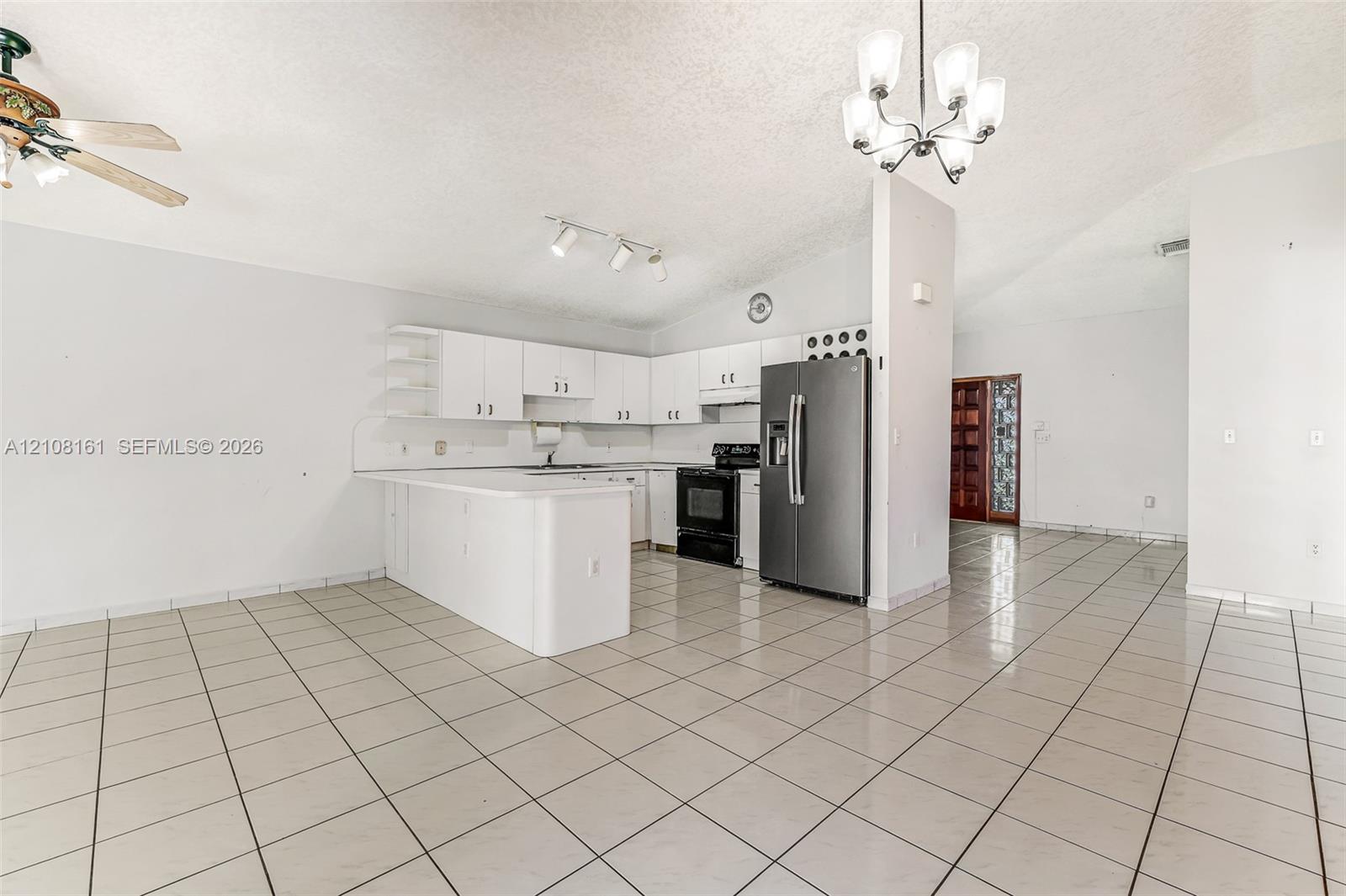 Kitchen featuring white cabinetry, a peninsula, tile flooring, stainless steel refrigerator, and vaulted ceilings with multi-light fixture