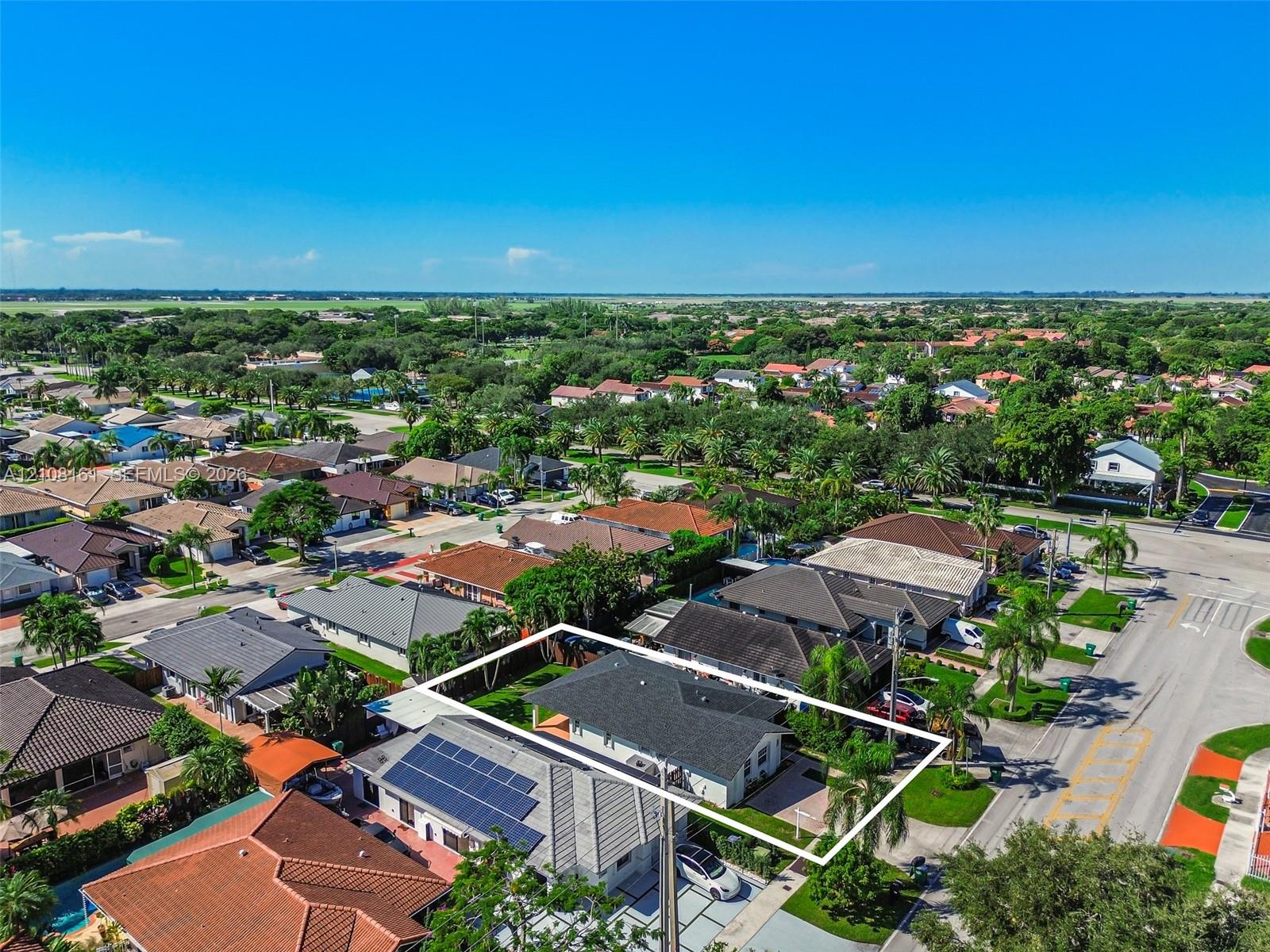 Aerial perspective of a residential property featuring a dark-toned pitched roof, a fenced perimeter, integrated solar panel array, and paved driveway
