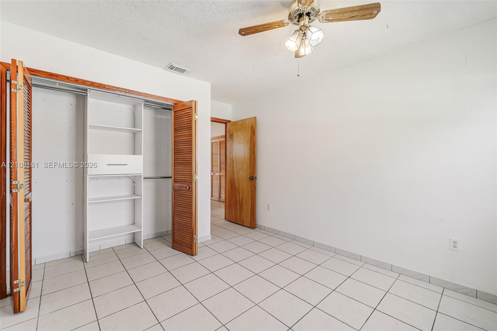 Room featuring ceramic tile flooring, a dual-door closet with built-in shelving, a natural wood-finish interior door, and a multi-light ceiling fan