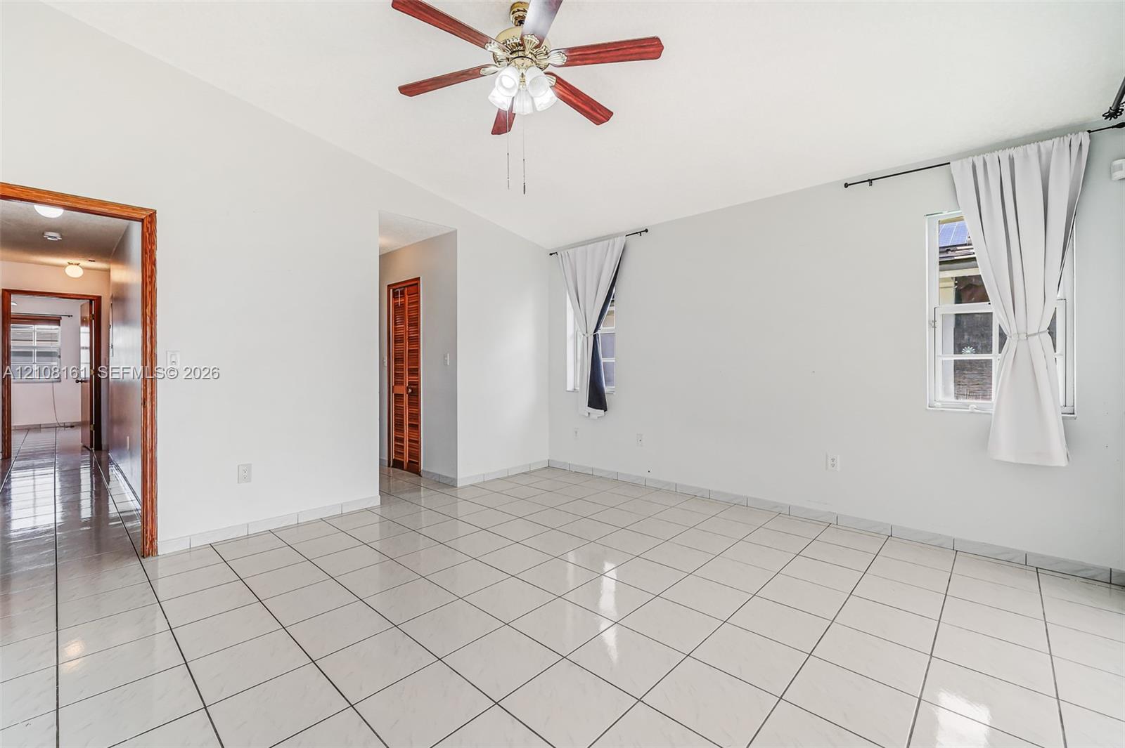 Interior space featuring light-colored tile flooring, vaulted ceilings, and a central ceiling fan with multi-light fixture