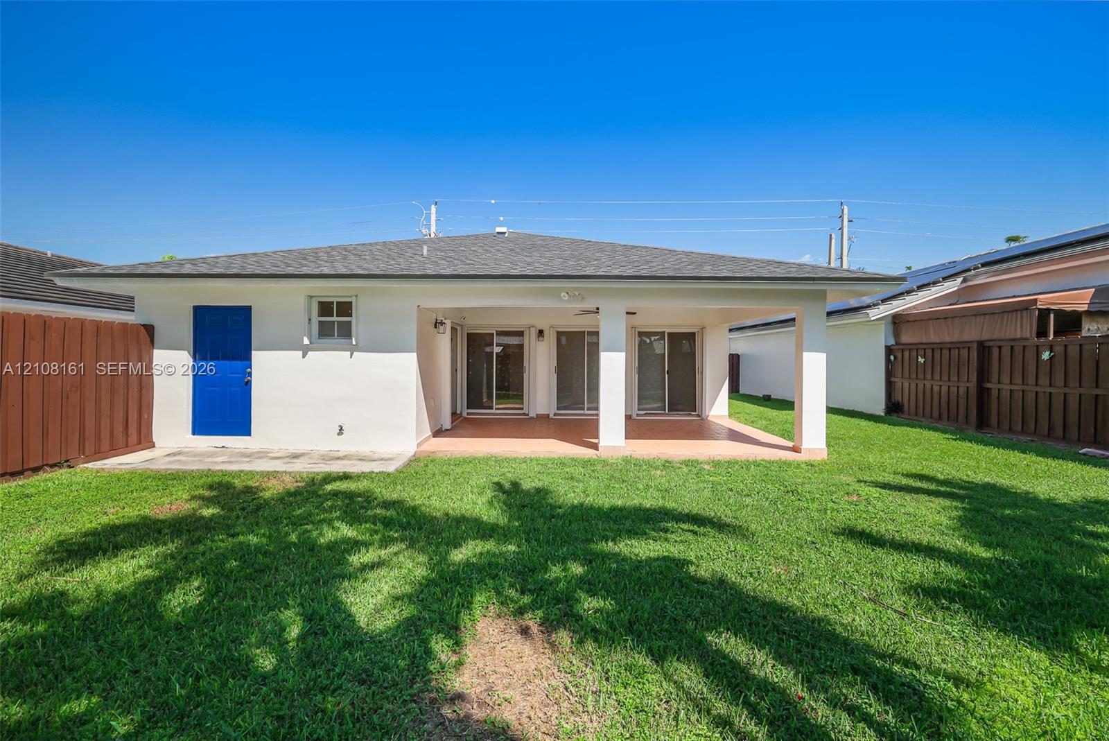 Covered rear patio featuring tile flooring, multi-panel sliding glass doors, and a manicured lawn enclosed by wood fencing