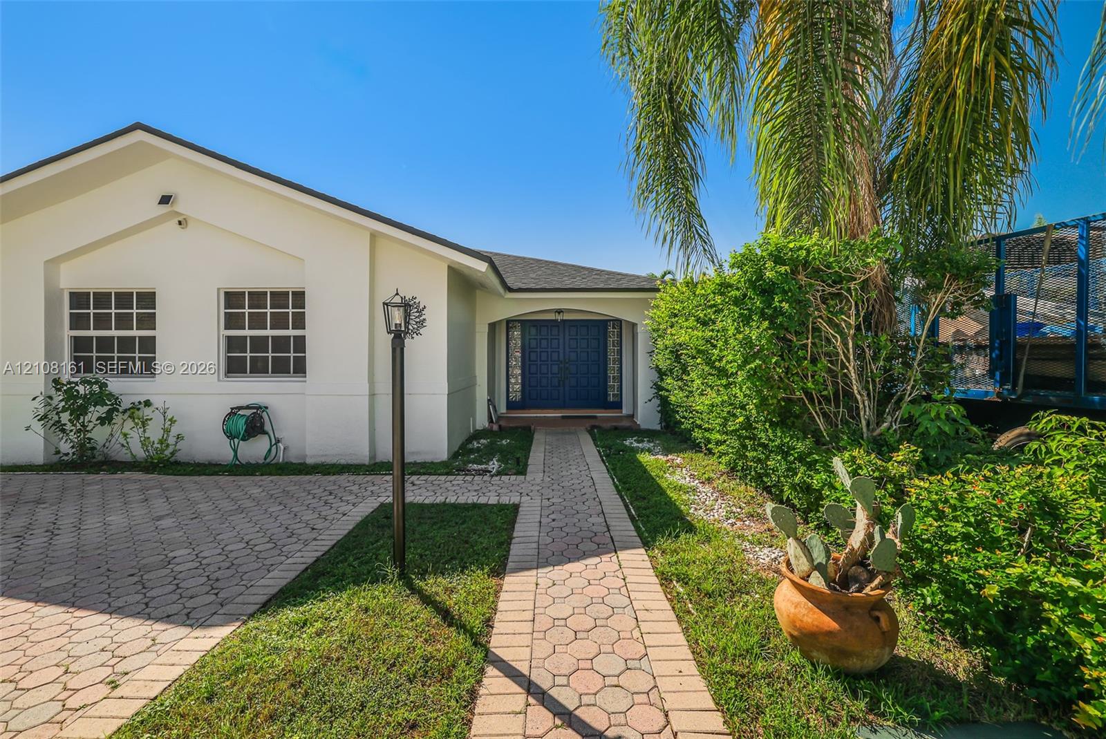 Single-story exterior featuring a light-toned stucco faade, decorative double-entry doors, a paver driveway, and a paved walkway