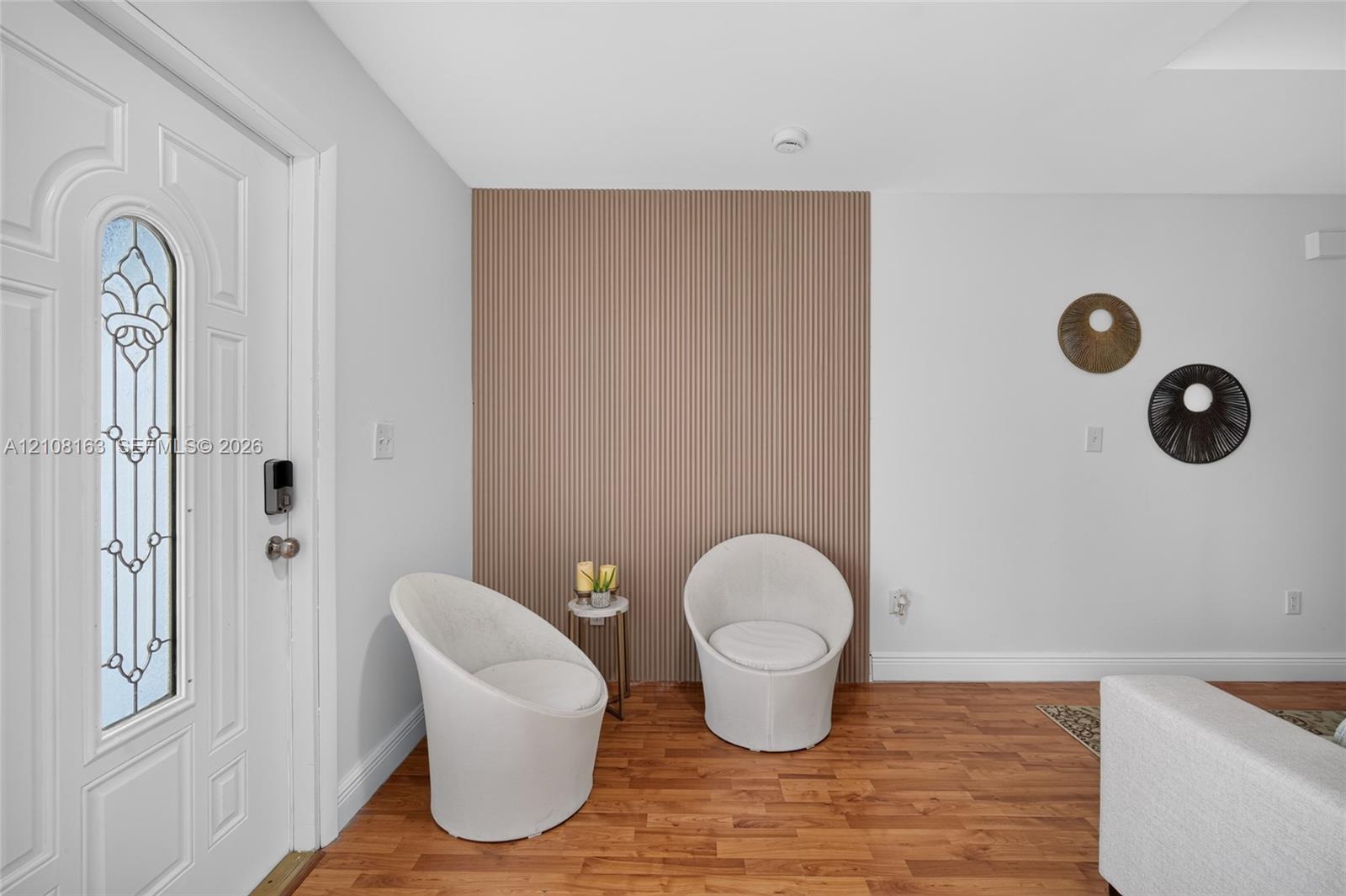 Entryway featuring a front door with decorative glass insert, wood-finish flooring, and a floor-to-ceiling vertical slatted wood-finish accent wall