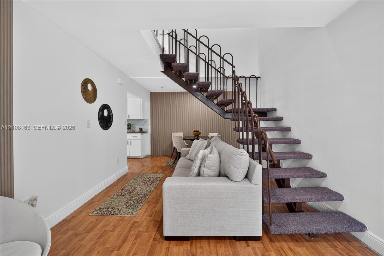 Open-riser staircase with carpeted treads and decorative metal railing, wood-finish flooring, and vertical accent paneling