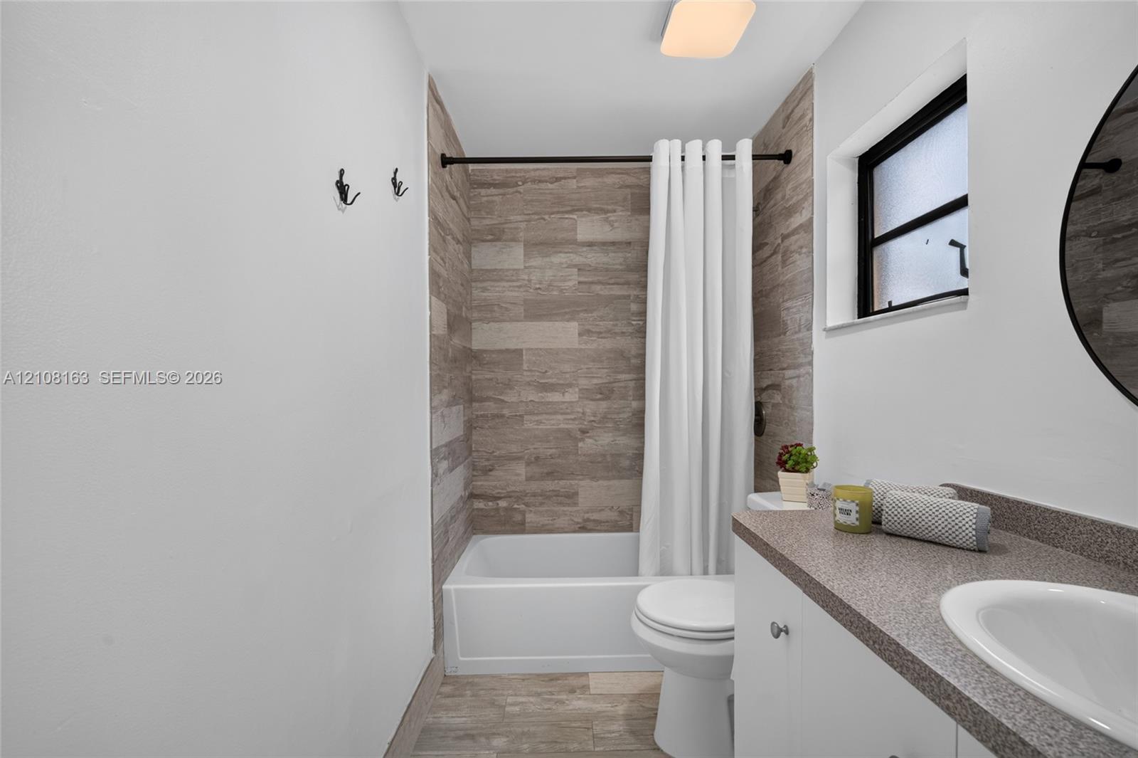 Bathroom featuring a stone-finish tile tub surround, white vanity cabinet with a stone-finish countertop, undermount sink, and wood-finish tile flooring
