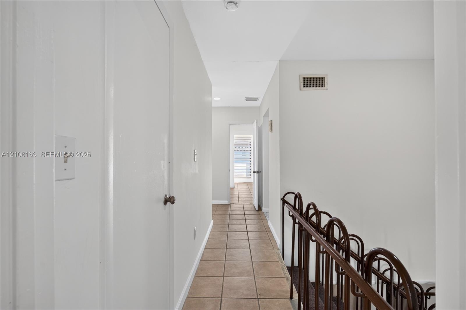 Hallway featuring neutral tile flooring and a decorative metal stair railing