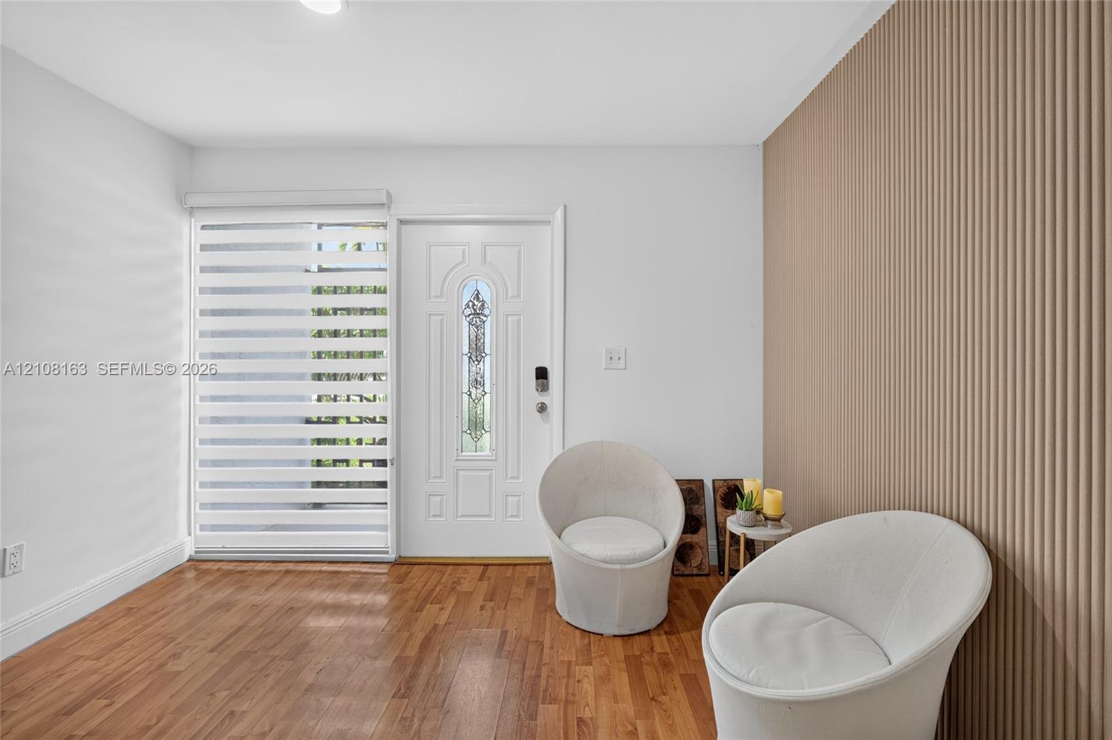 Entry featuring wood-finish flooring, a decorative textured wall treatment, a panel door with a decorative glass insert, and adjustable horizontal window treatments