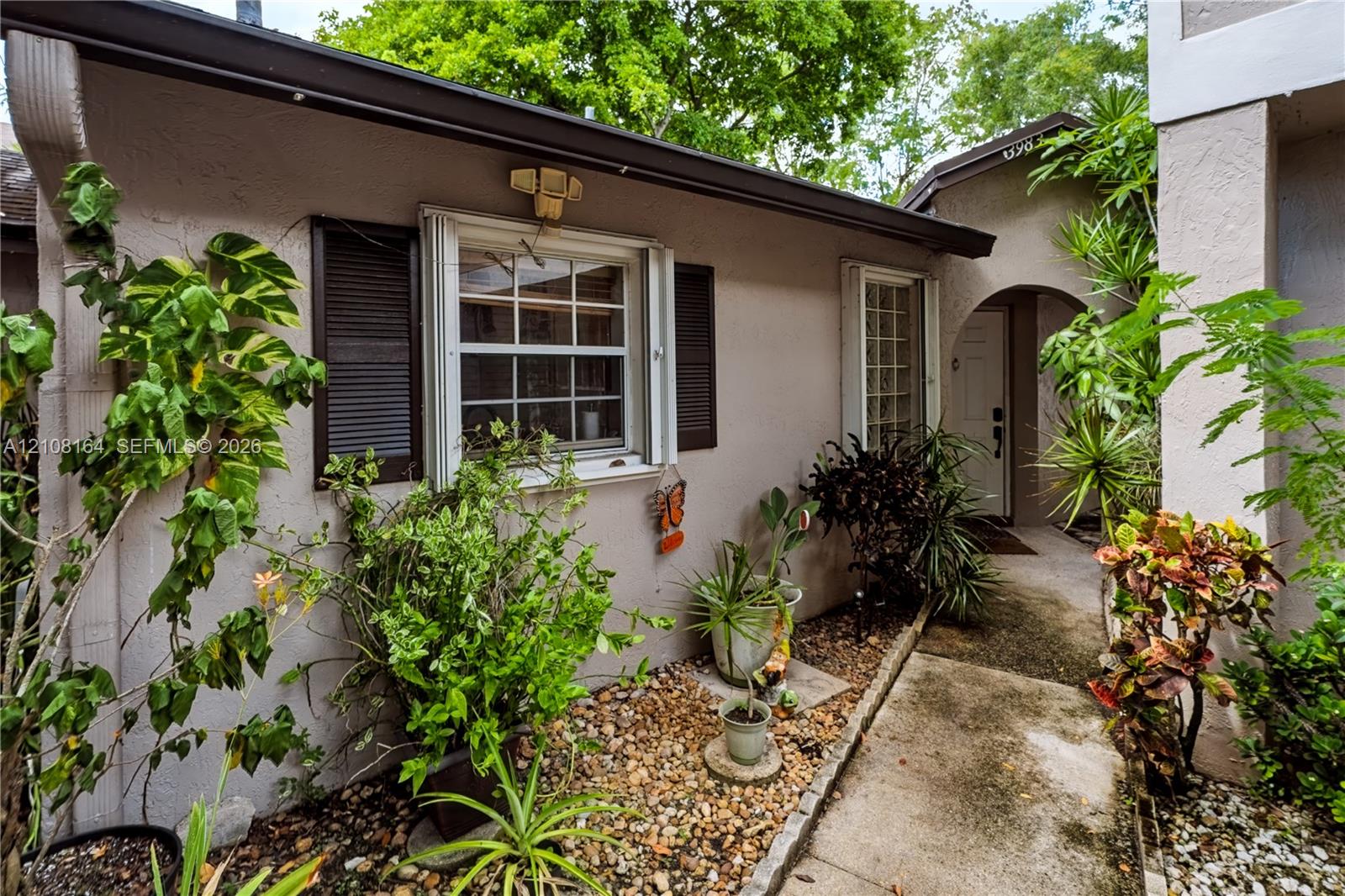 Stucco exterior featuring dark-toned window shutters, an arched entryway, and a concrete pathway