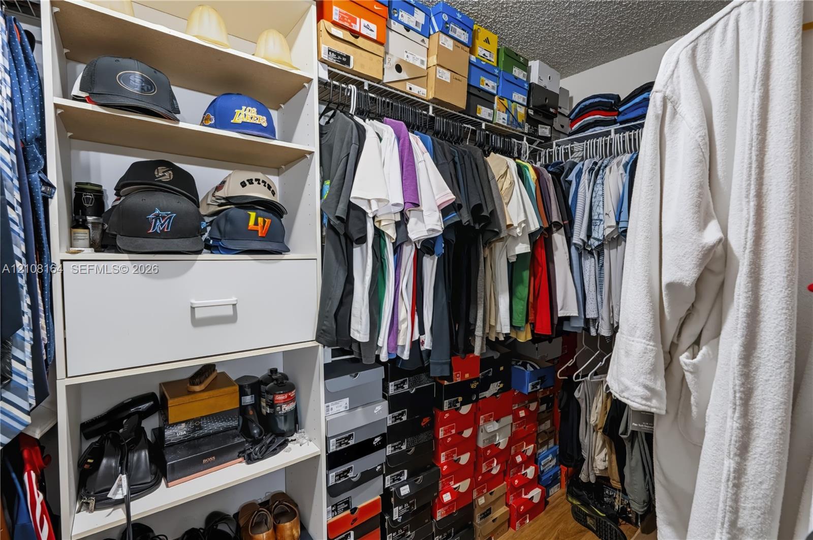 Walk-in closet featuring white laminate built-in cabinetry, an integrated pull-out drawer, adjustable open shelving, and multi-level metal hanging rods
