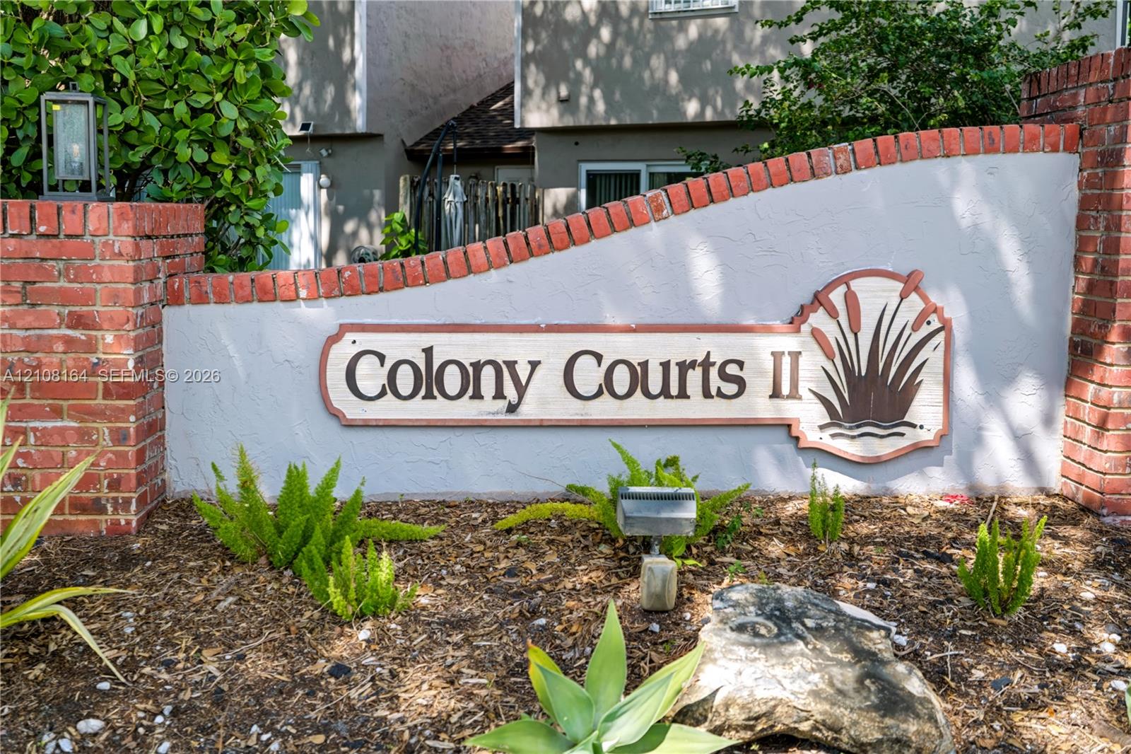 Stucco monument sign featuring brick pillars, integrated landscape lighting, and curated garden beds