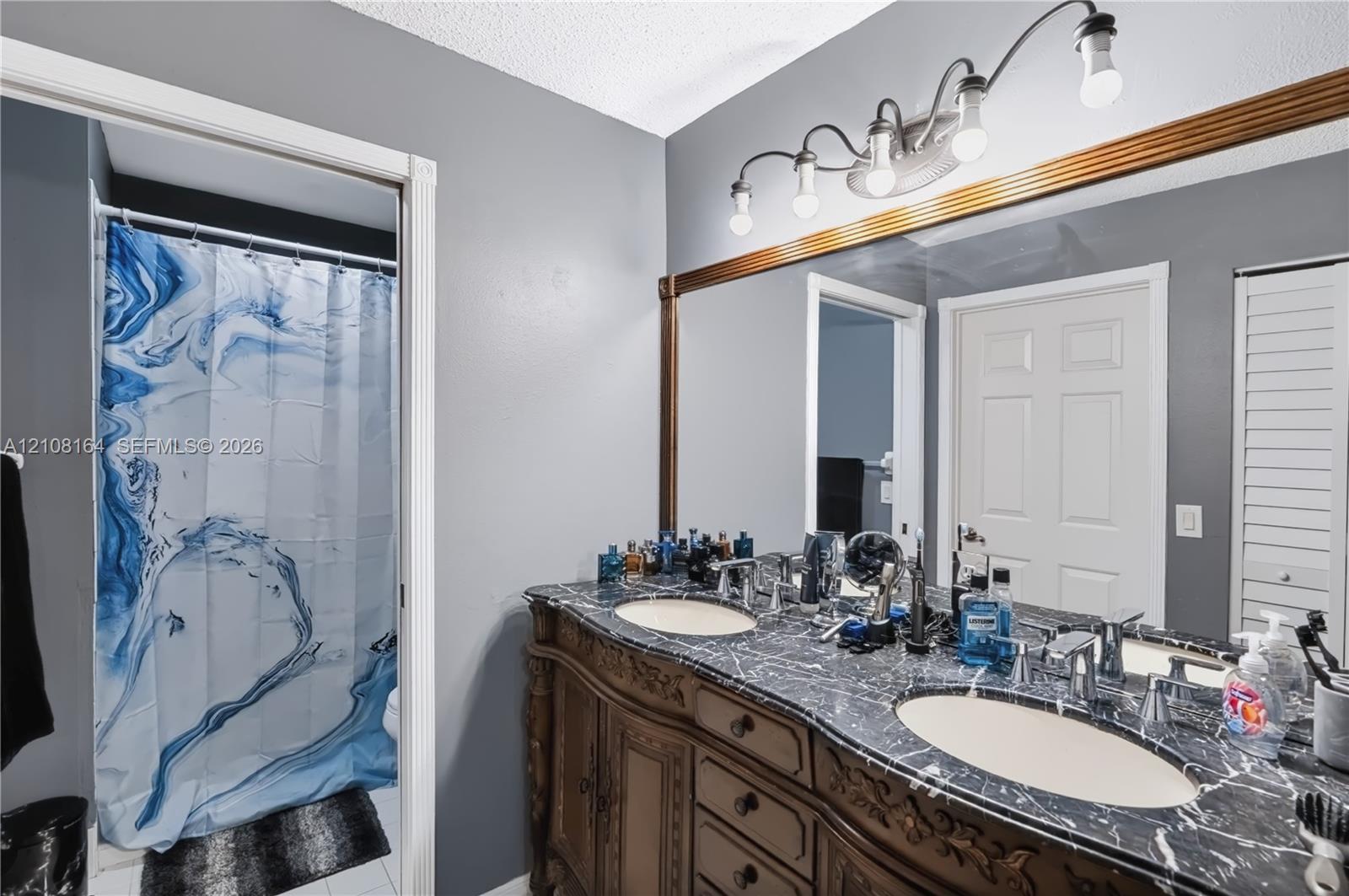 Custom wood cabinetry with ornate detailing, dual under-mount sinks, stone-finish countertops, full-width wall mirror with wood trim, and multi-light vanity fixture