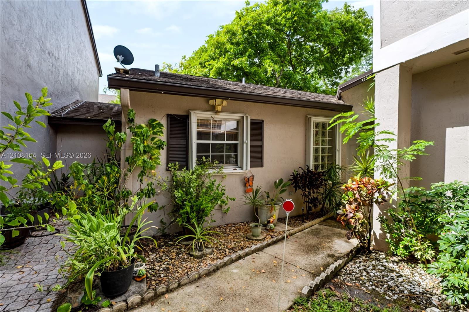 Stucco exterior featuring dual-pane windows, dark shutter accents, exterior lighting, and a stone-paver walkway