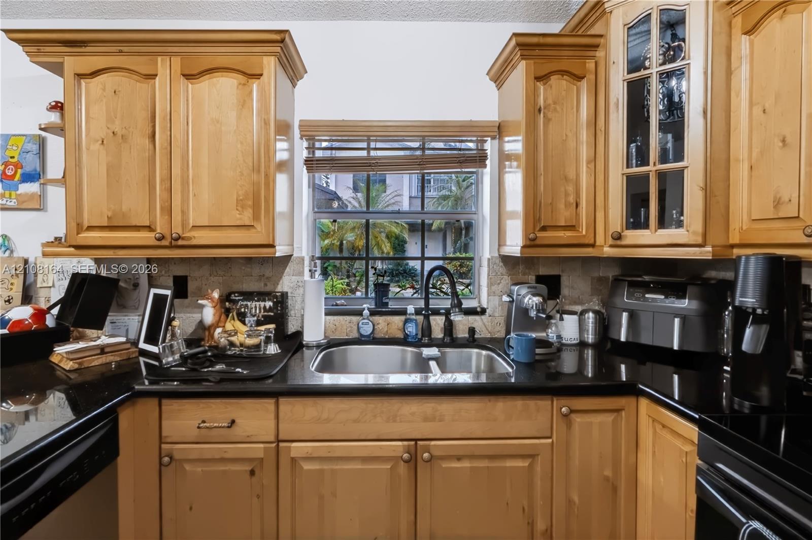 Kitchen featuring natural wood cabinetry with crown molding, black stone countertops, stone-tile backsplash, and glass-paneled upper cabinet doors
