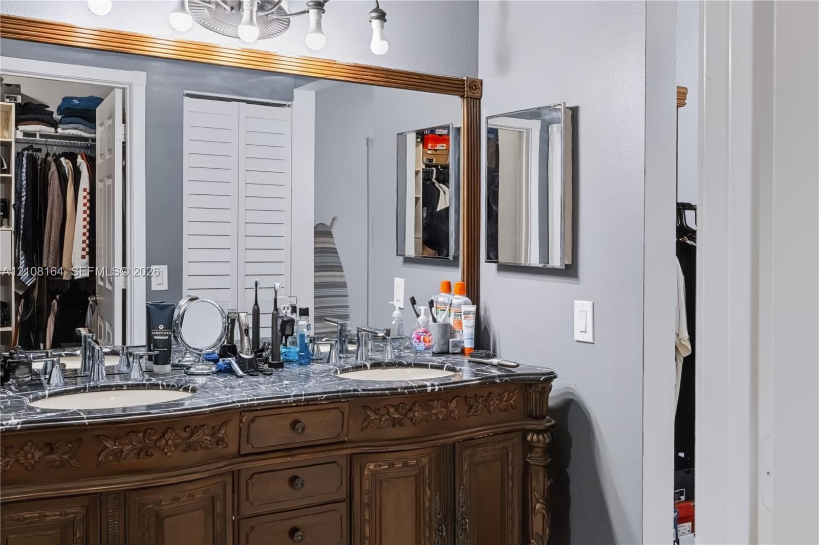 Double vanity featuring a stone countertop, dual undermount sinks, intricate wood cabinetry with carved detailing, and a wall-to-wall framed mirror