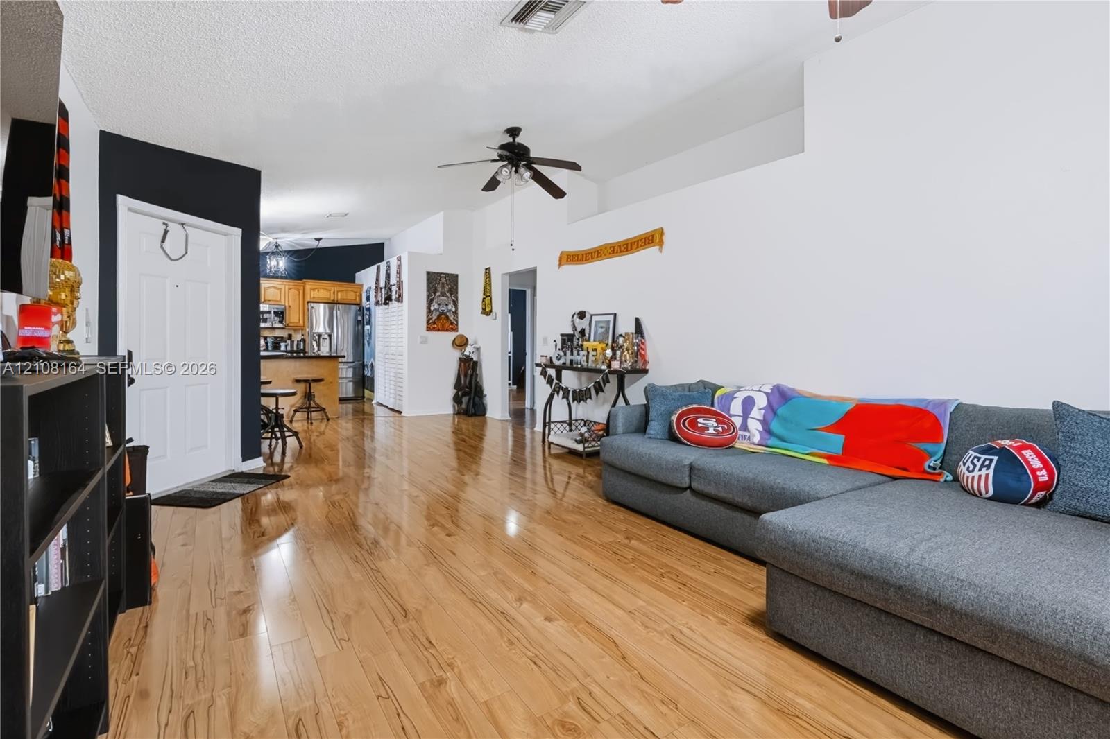 High-gloss wood-finish flooring, vaulted ceilings, and a ceiling fan, featuring a kitchen with wood cabinetry and an island