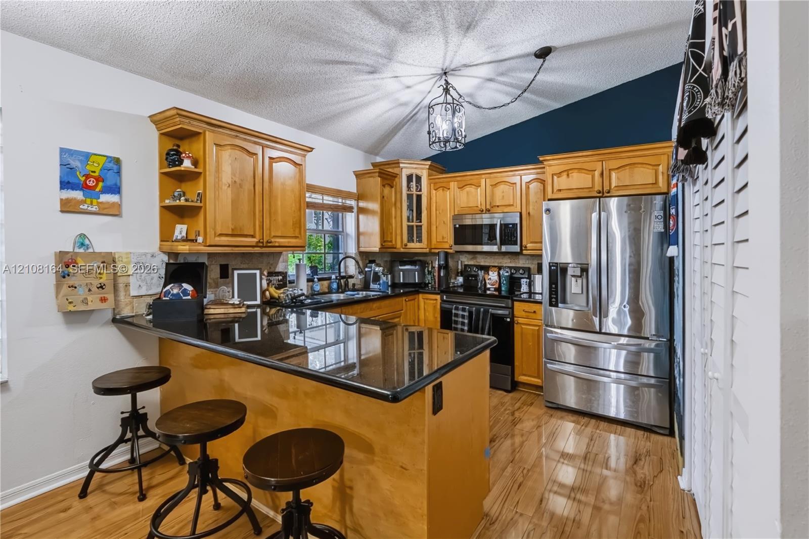Kitchen featuring wood cabinetry, dark stone-finish countertops, stainless steel appliances, wood-finish flooring, and a vaulted ceiling