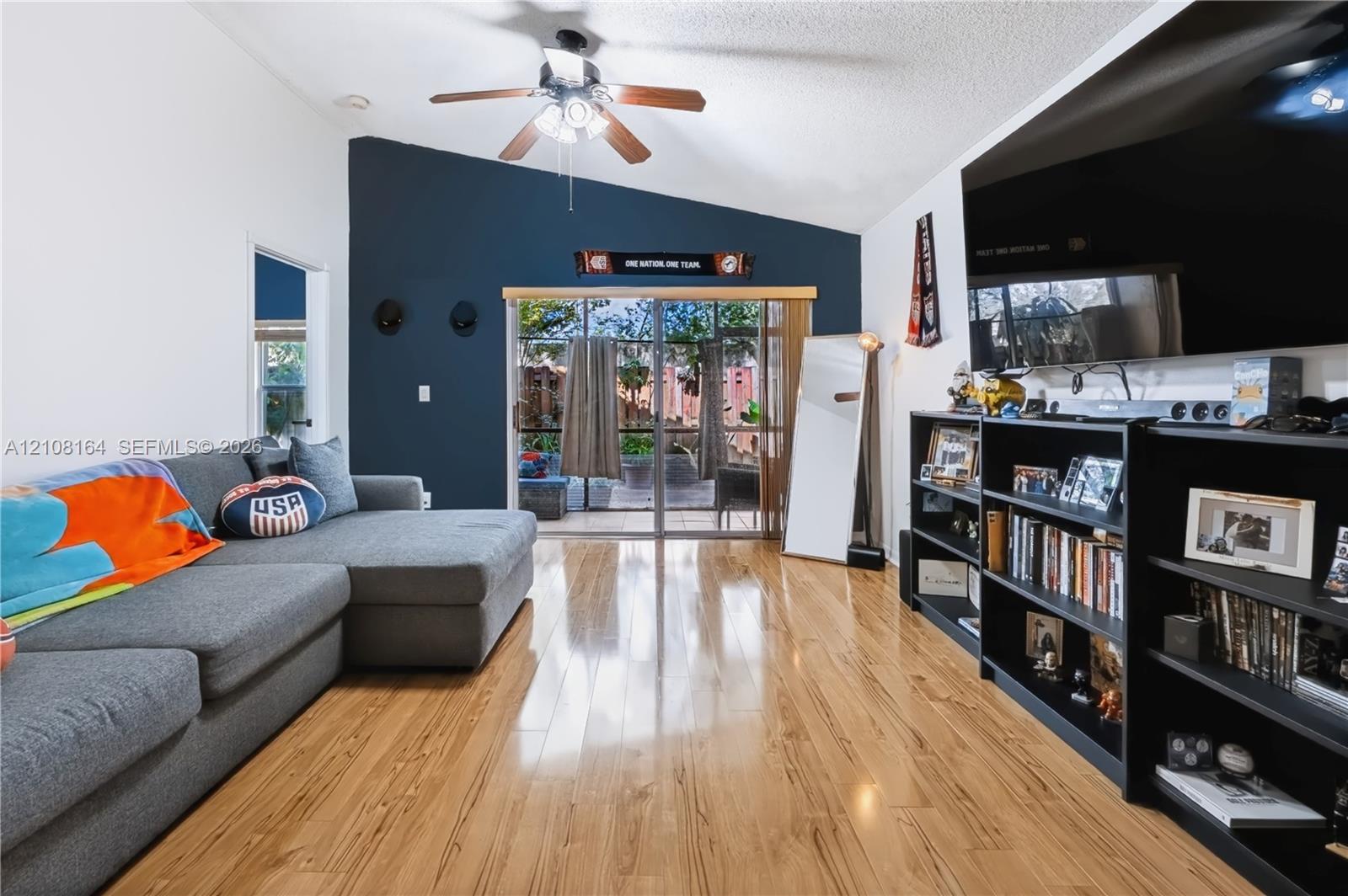 Vaulted ceilings, wood-finish flooring, accent wall, and sliding glass doors